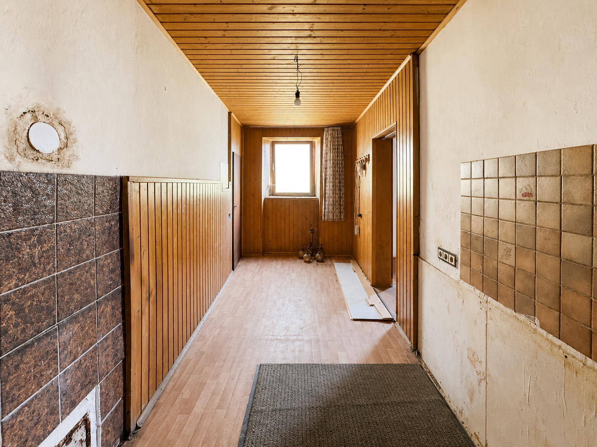 Flur mit Holzvertäfelung, Fliesen im unteren Bereich und einem Fenster am Ende des Ganges.