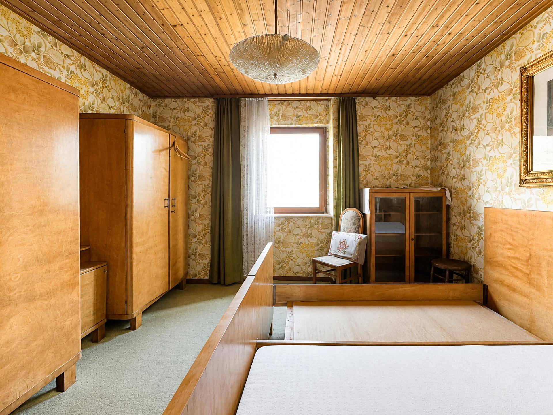 Schlafzimmer im Vintage-Stil mit gemusterter Tapete, Holzdecke und klassischen Holzmöbeln.