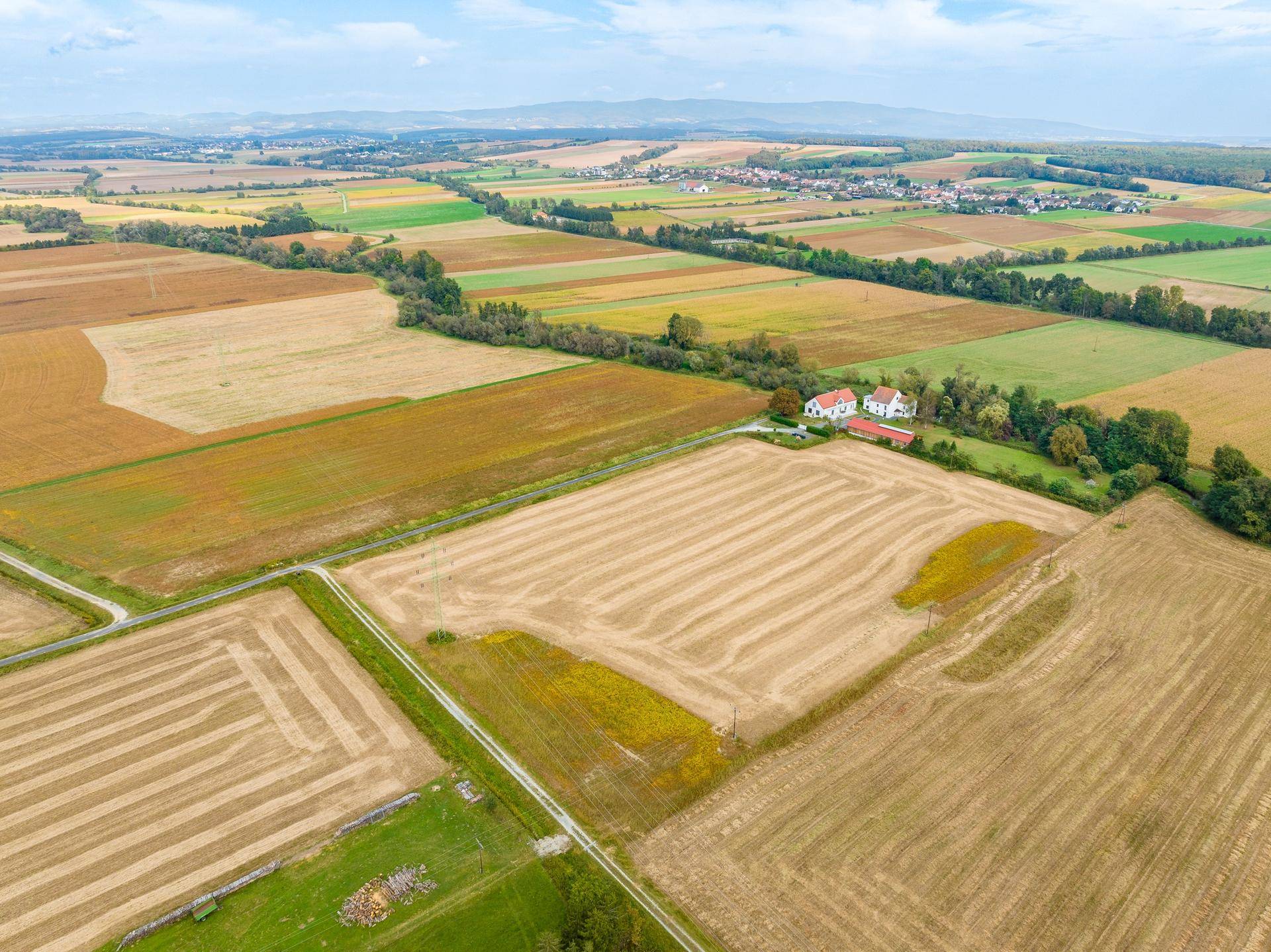 Weitläufige Luftaufnahme der ländlichen Umgebung mit Feldern, Wäldern und Bergen am Horizont.