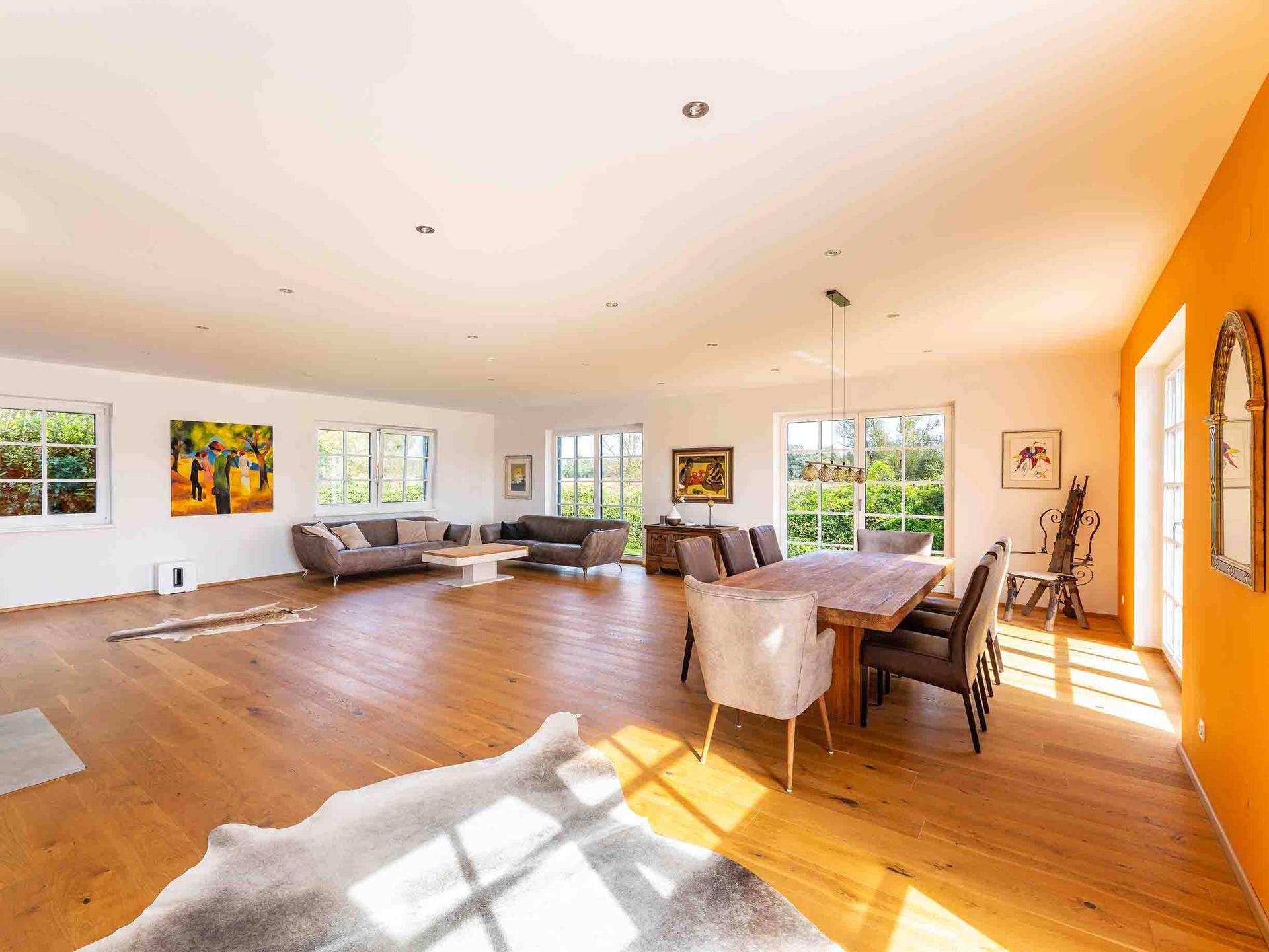 Großzügiger Wohn- und Essbereich mit Holzboden, vielen Fenstern und einer farbigen Akzentwand.