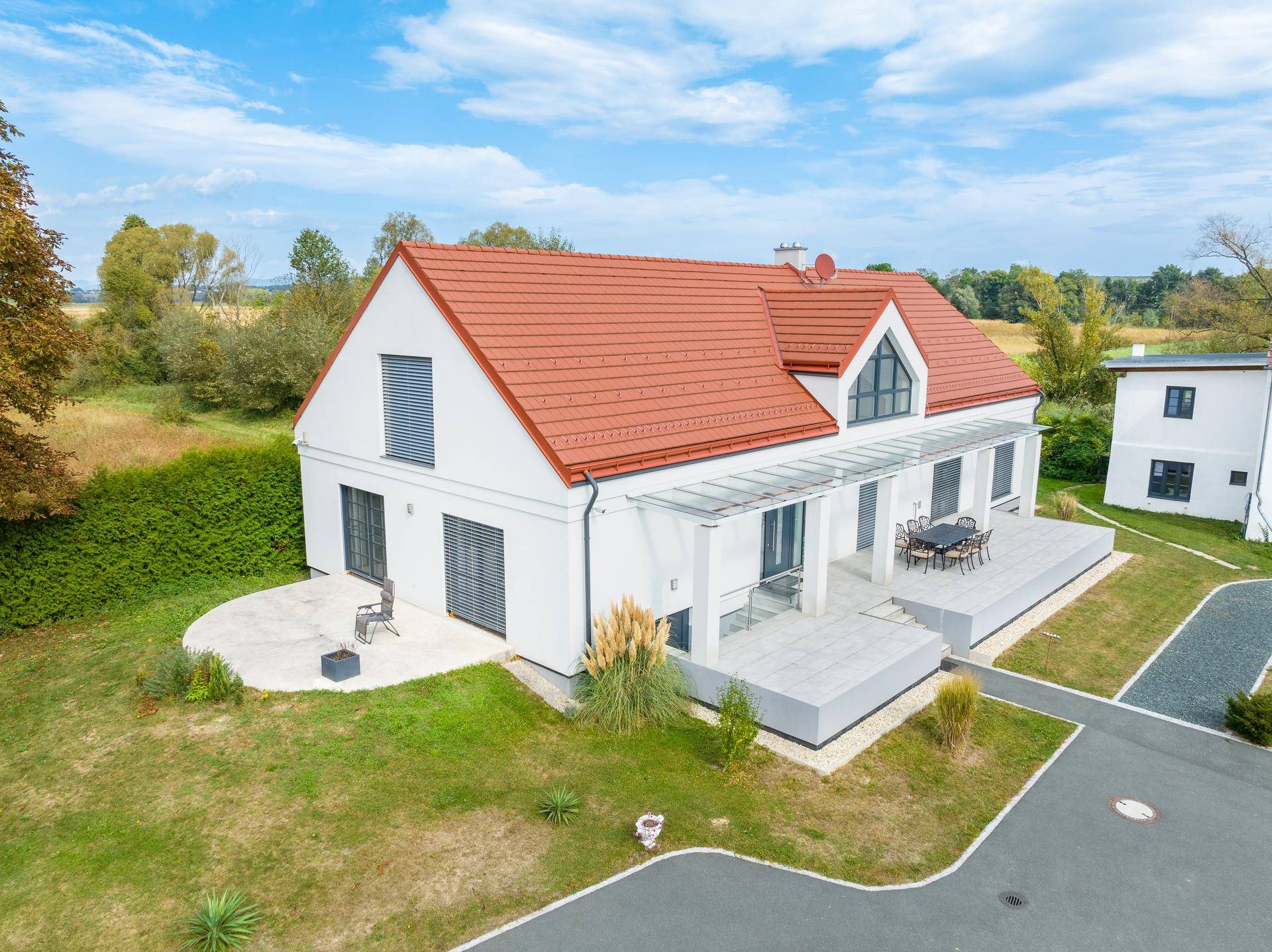 Moderne Villa mit großer, möblierter Terrasse und gepflegtem Rasen, umgeben von ländlicher Natur.