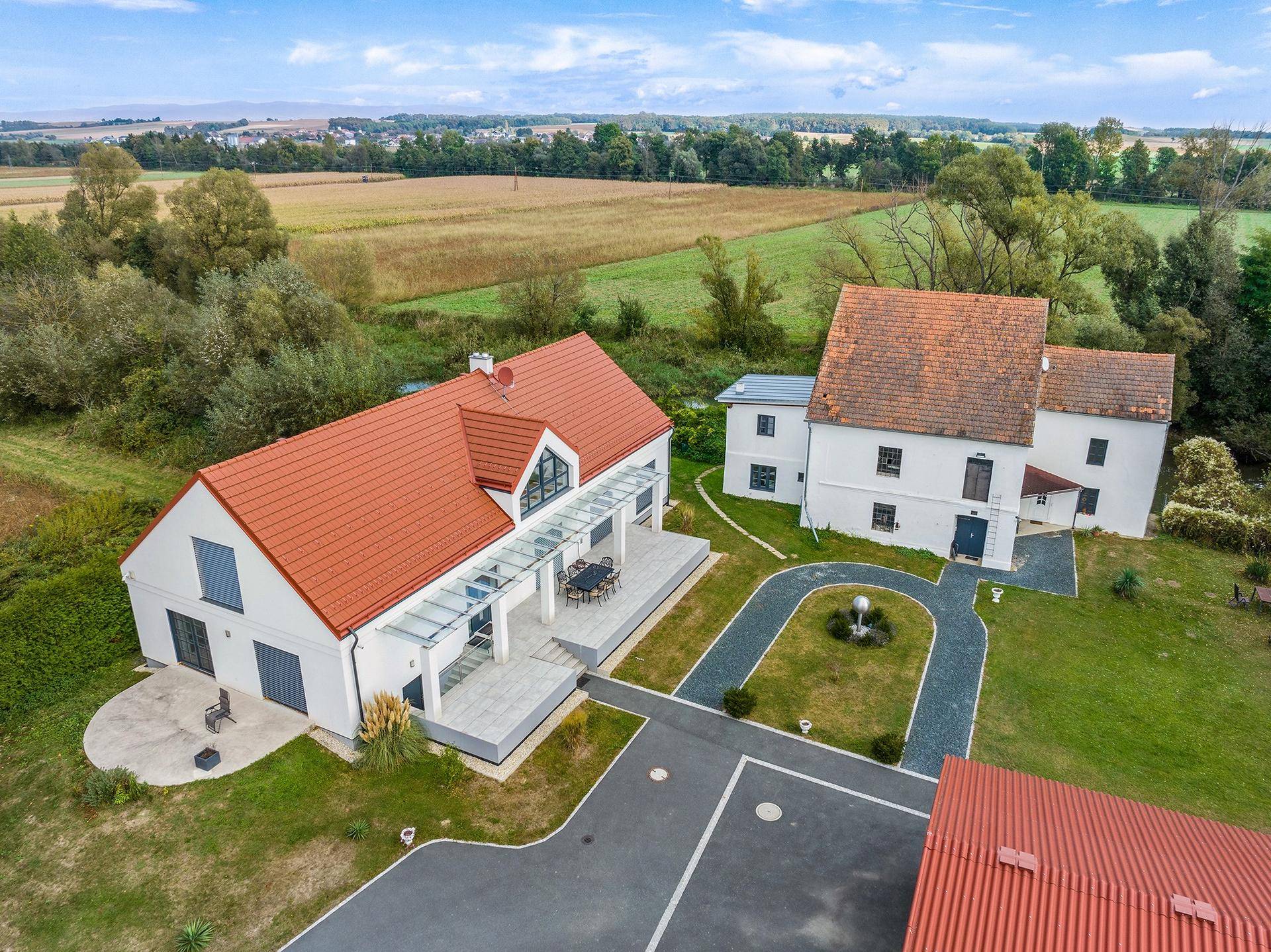 Luftaufnahme des Anwesens mit zwei Gebäuden, einer modernen Villa und einem historischen Mühlengebäude.