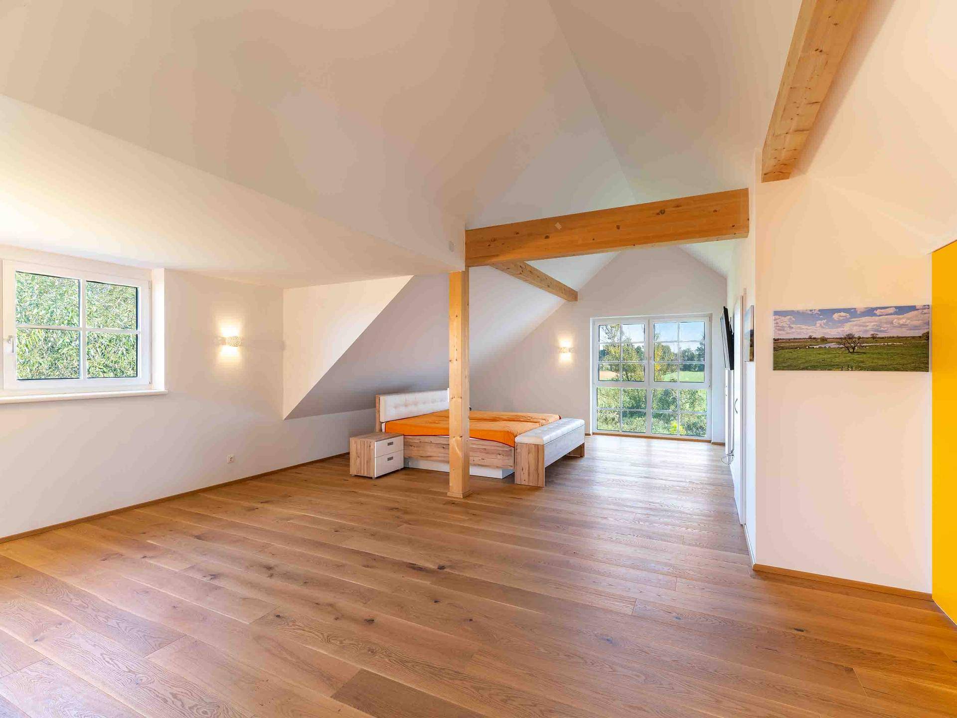 Großes Schlafzimmer im Dachgeschoss mit Holzboden, sichtbaren Holzbalken und weitem Ausblick.