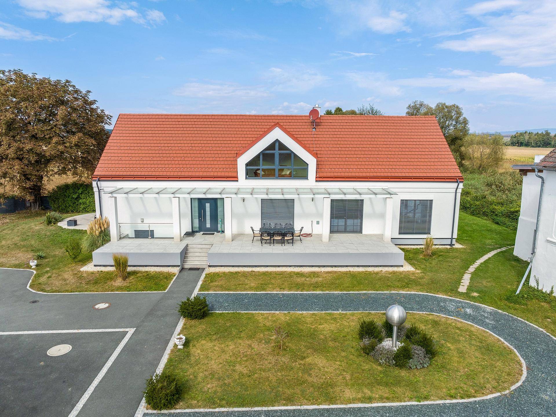 Ansicht der modernen Villa mit großer Terrasse, gepflegter Auffahrt und weitem Blick ins Grüne.