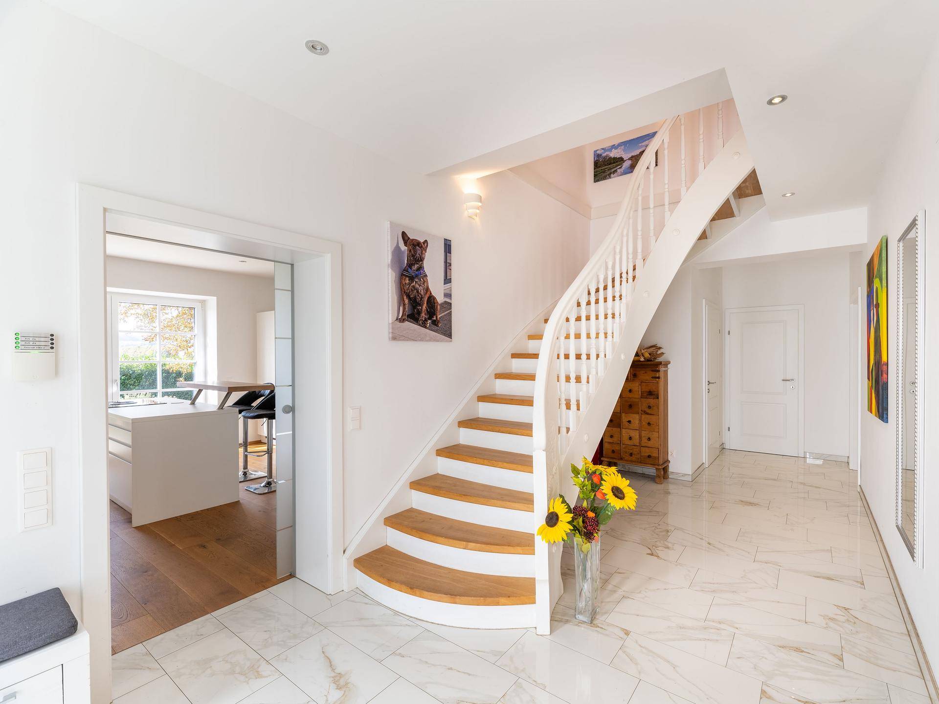 Heller Flur mit eleganter geschwungener Treppe, Marmorfliesenboden und Zugang zur Küche.