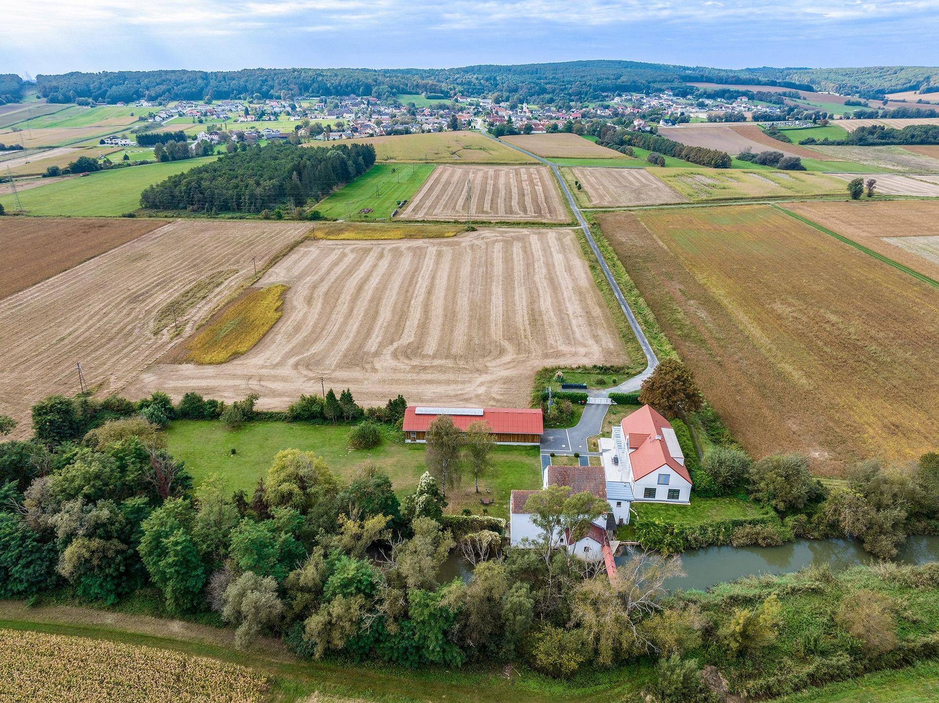 Weitläufige Luftaufnahme des Anwesens mit angrenzenden Feldern und einem Dorf in der Ferne.