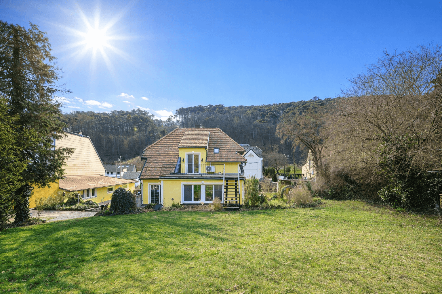 Rückansicht des Hauses mit großem, sonnigem Garten und umgebenden Bäumen.