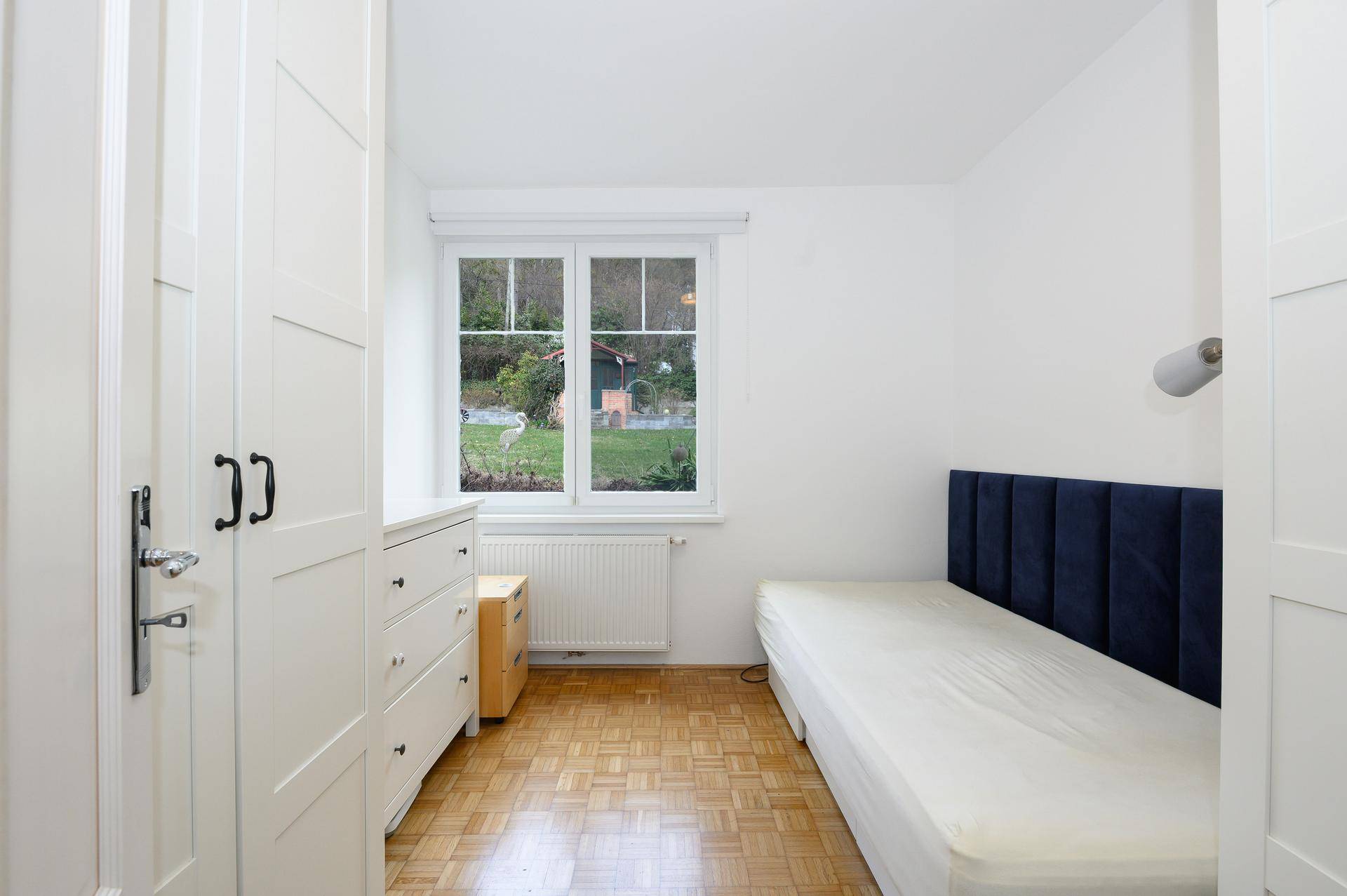 Gemütliches Schlafzimmer mit Einzelbett, weißem Kleiderschrank und Blick in den Garten.