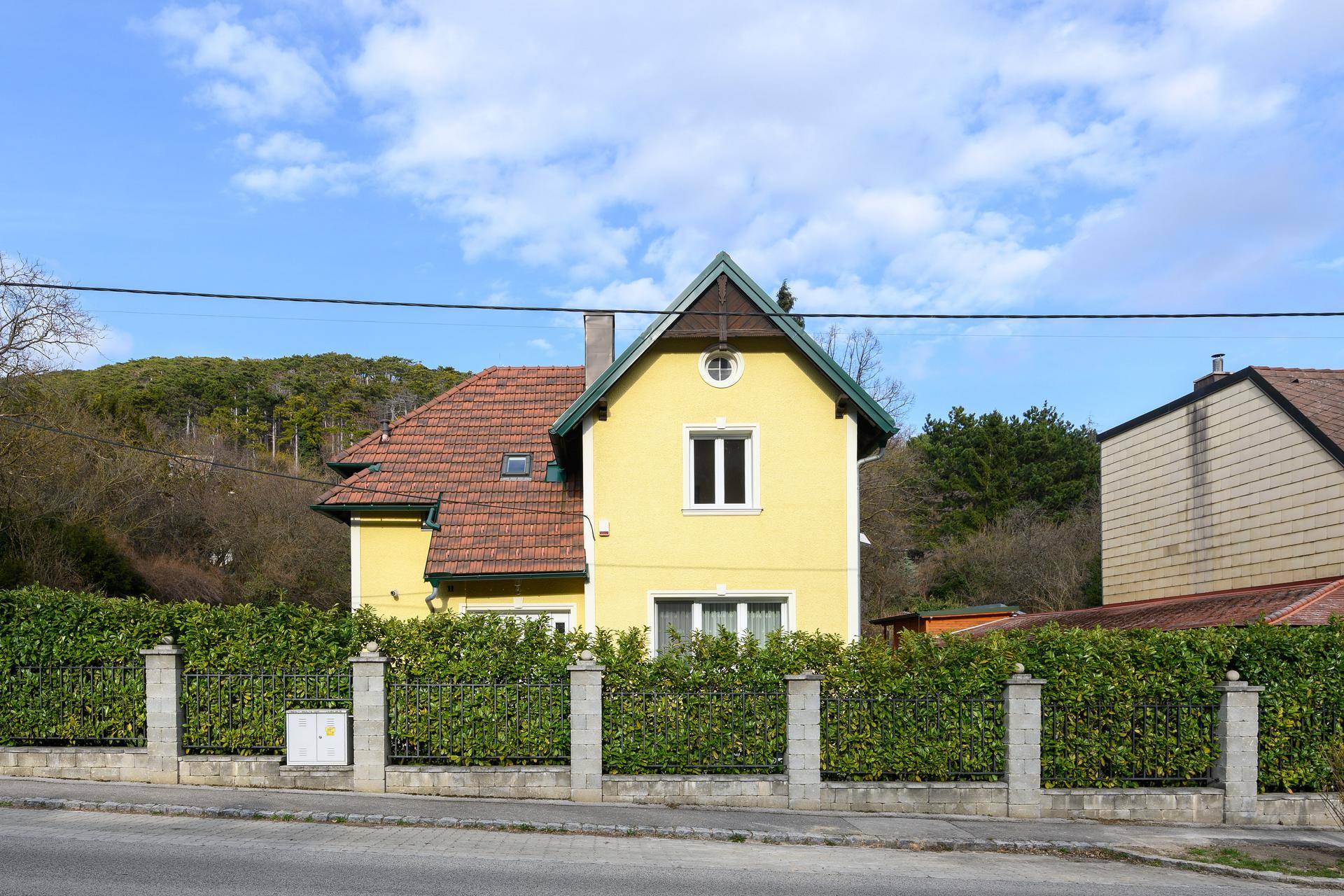 Ansicht des Hauses von der Straße mit grüner Hecke und Zaun im Vordergrund.