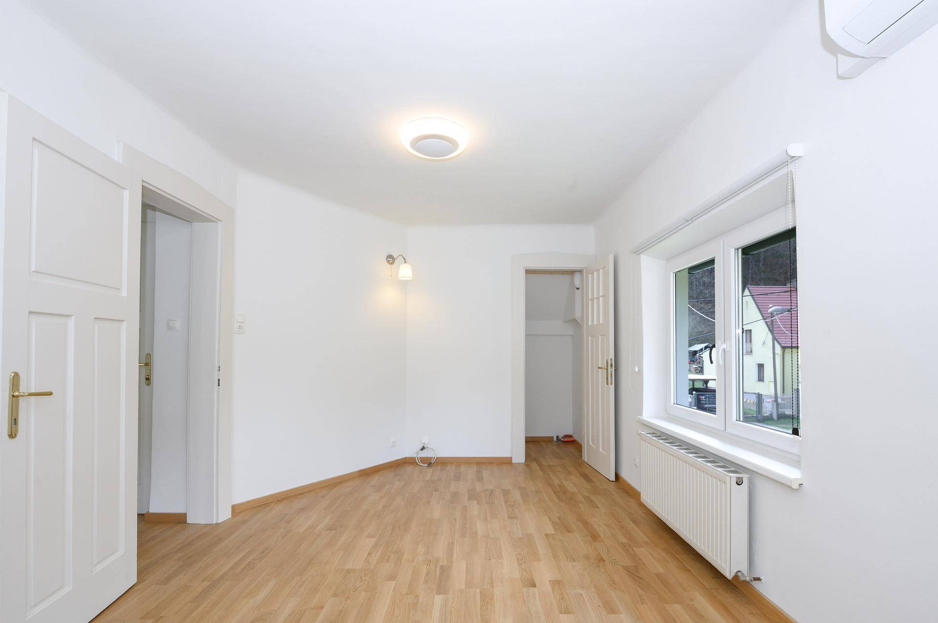 Helles Zimmer mit Holzboden, Klimaanlage und Fenster mit Blick auf die Umgebung.