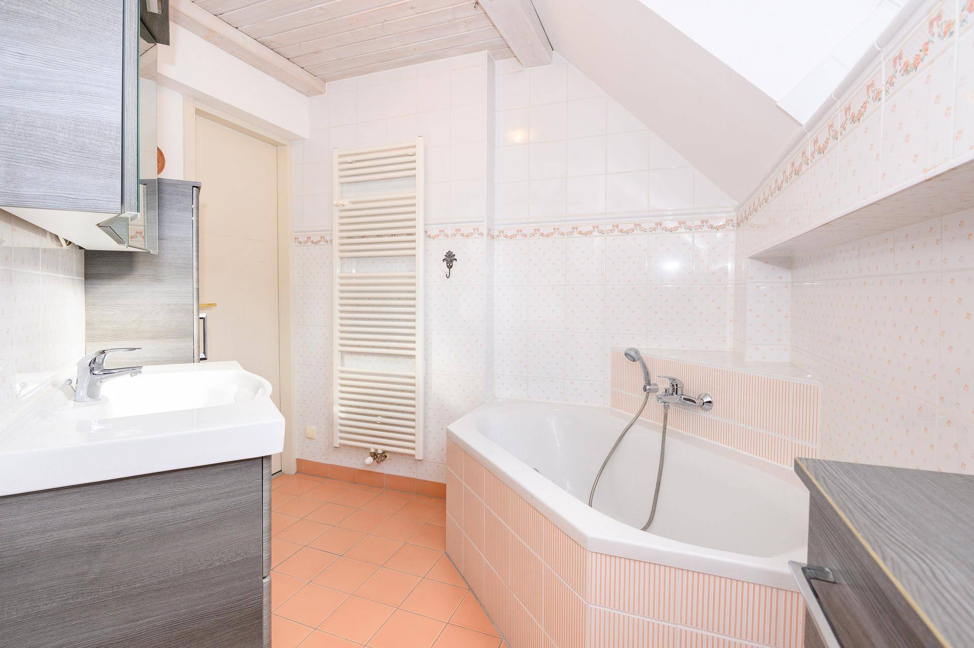 Badezimmer mit Badewanne, Waschbecken, Handtuchheizkörper und Dachschräge.
