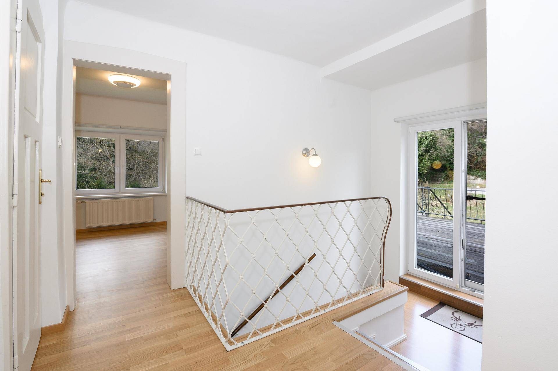 Heller Flur mit Holztreppe und Zugang zu einem Außenbereich mit Blick ins Grüne.