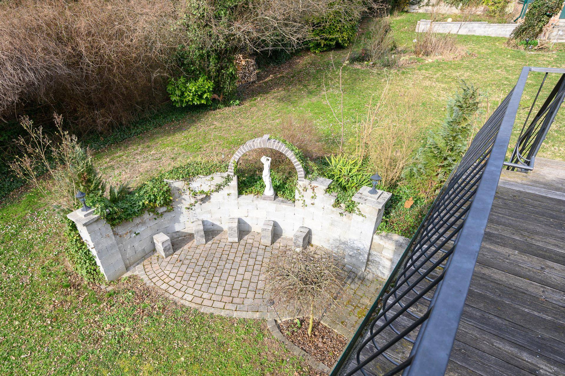 Gepflasterte Terrasse mit Steinmauer und Statue, von oben betrachtet.