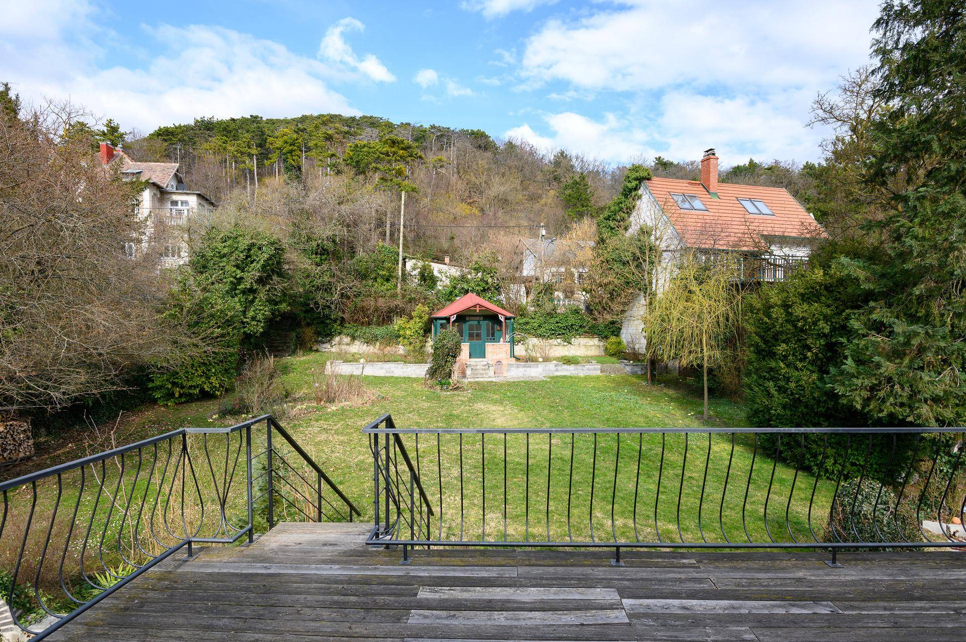 Holzbalkon mit Blick auf den weitläufigen Garten und ein Gartenhaus im Hintergrund.