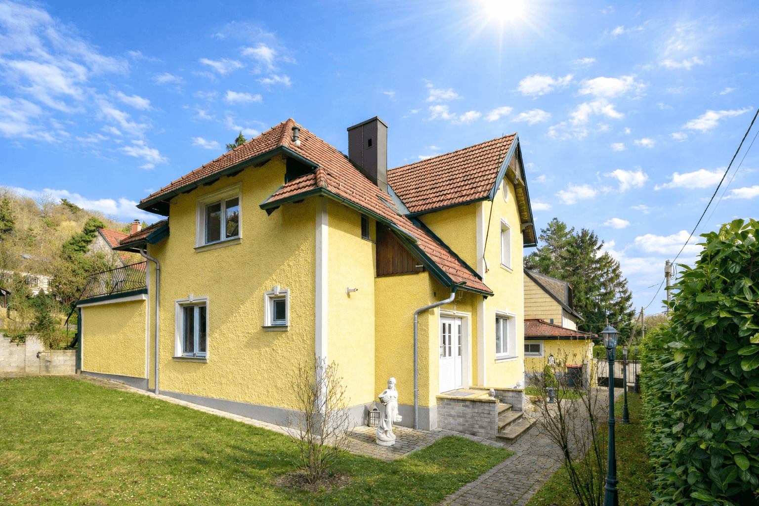 Sonniges gelbes Haus mit rotem Ziegeldach und gepflegtem Rasen im Vordergrund.
