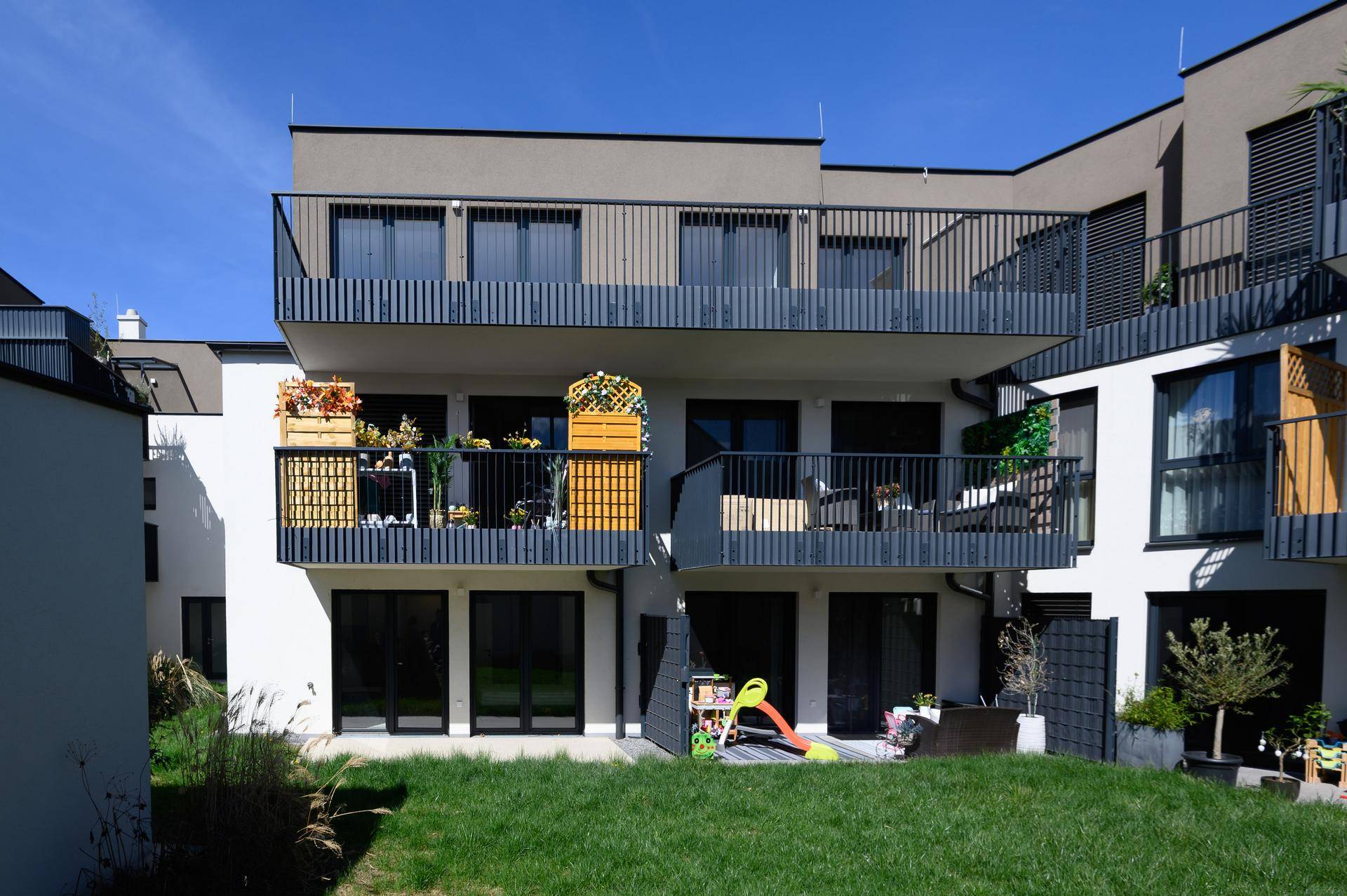 Moderne Wohnanlage mit mehreren Balkonen, Terrassen und einem kleinen Gartenbereich mit Spielgeräten.