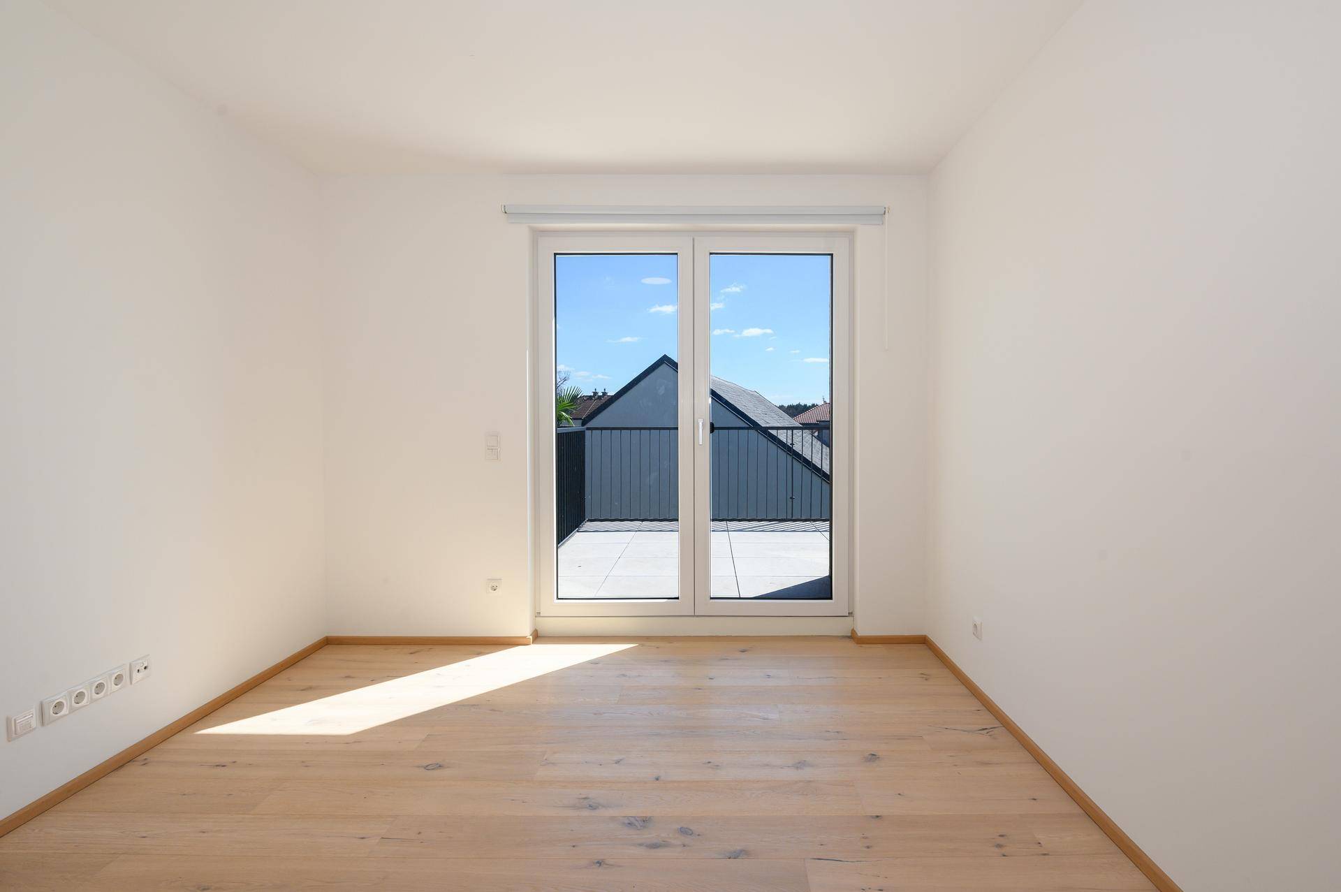 Helles Schlafzimmer mit Parkettboden und direktem Zugang zu einem sonnigen Balkon oder einer Terrasse.