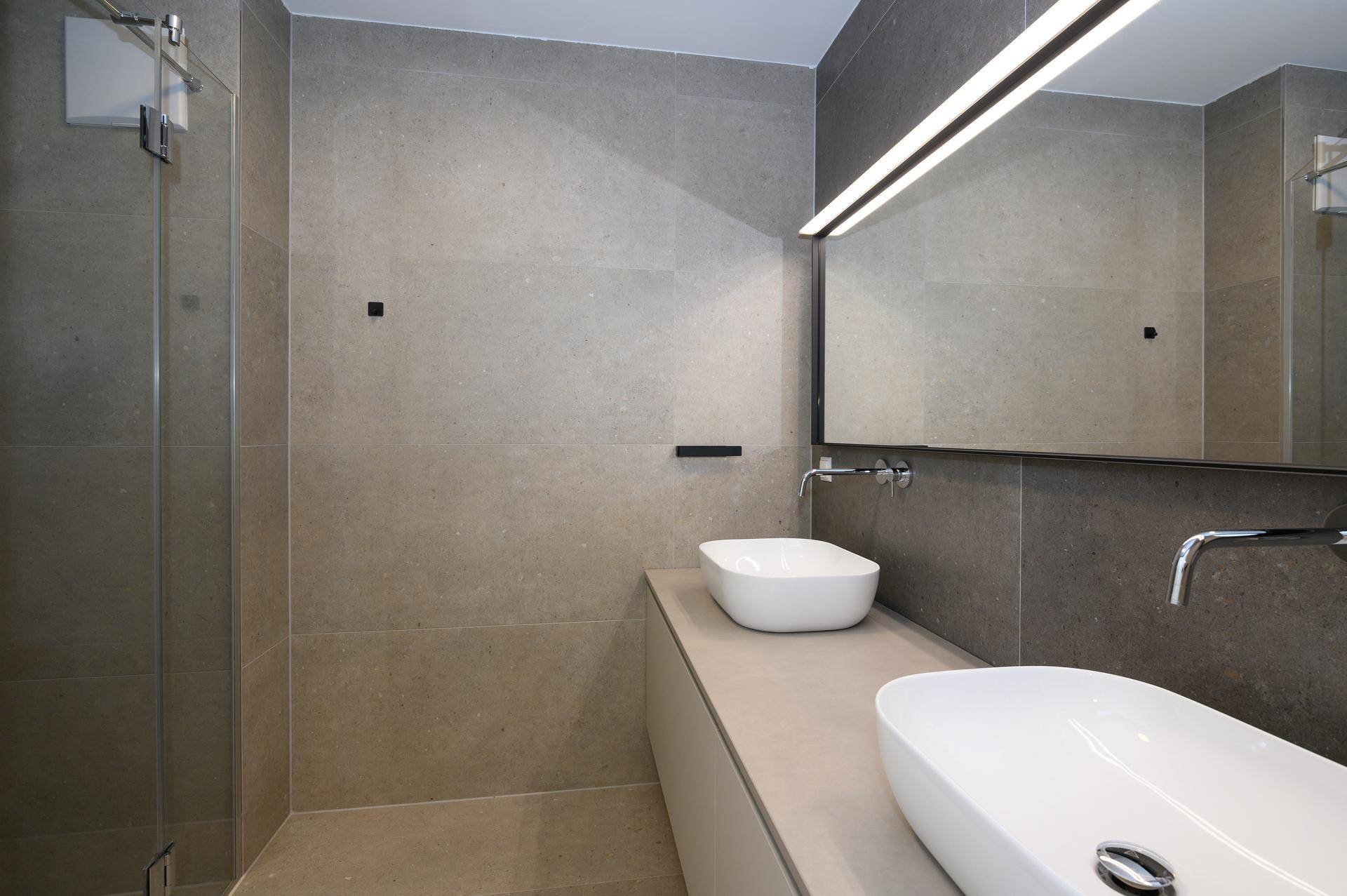 Modernes Badezimmer mit grauen Fliesen, Doppelwaschbecken und einer begehbaren Dusche.
