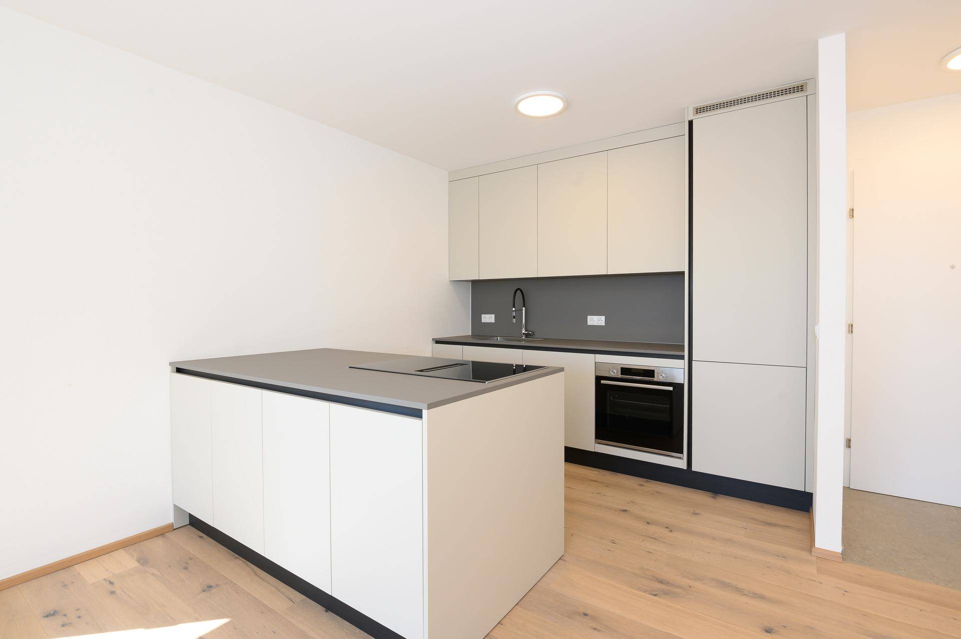 Moderne Einbauküche mit hellgrauen Schränken, Kochinsel und integrierten Geräten in neuwertigem Zustand.