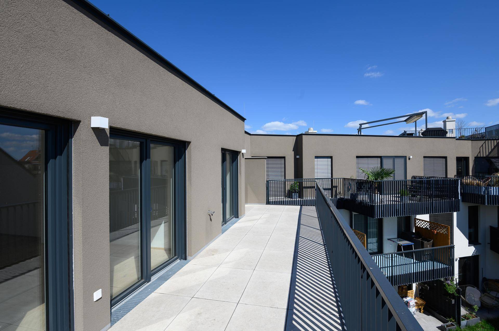 Geräumige Dachterrasse mit Fliesenboden und Blick auf die umliegenden Balkone der modernen Wohnanlage.