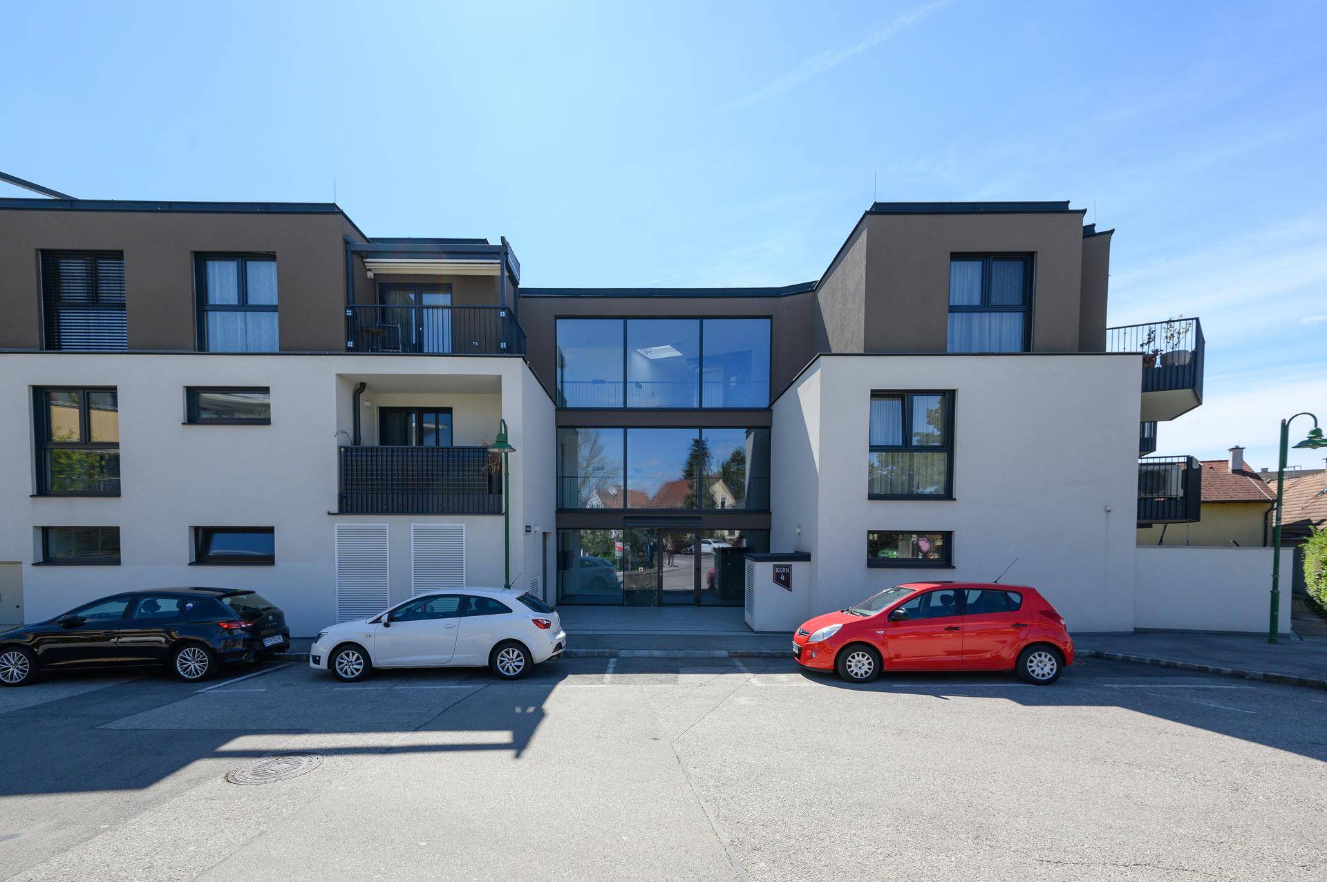 Moderne Wohnanlage mit ansprechender Fassade, großen Fenstern und Parkplätzen vor dem Gebäude.