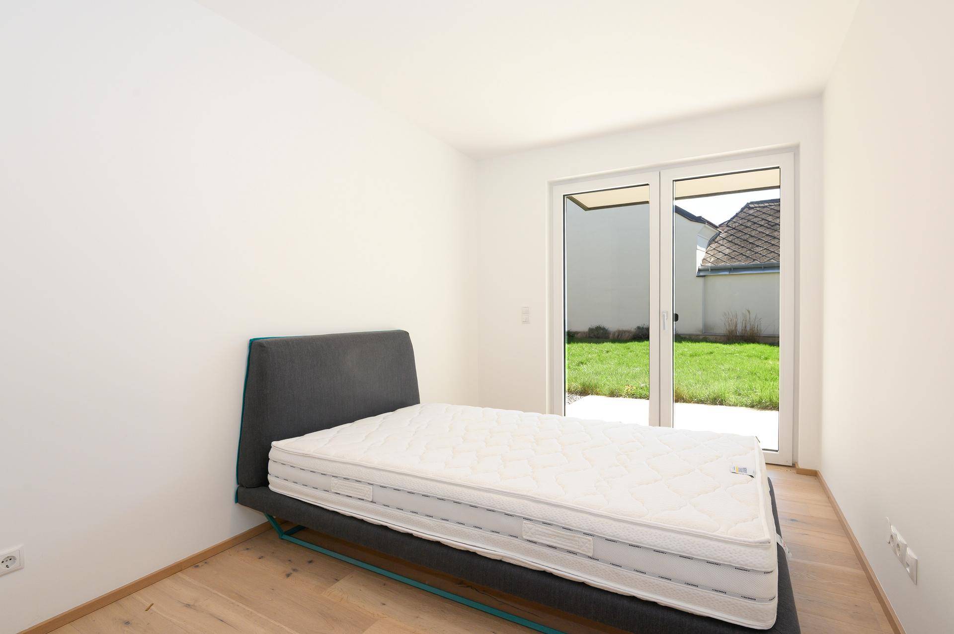 Helles Schlafzimmer mit Parkettboden und direktem Zugang zu einer kleinen Grünfläche.
