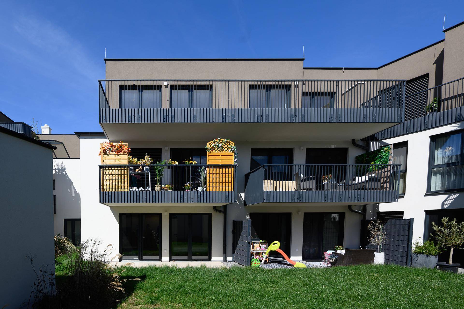 Moderne Wohnanlage mit Balkonen, Terrassen und gepflegter Rasenfläche im Außenbereich.