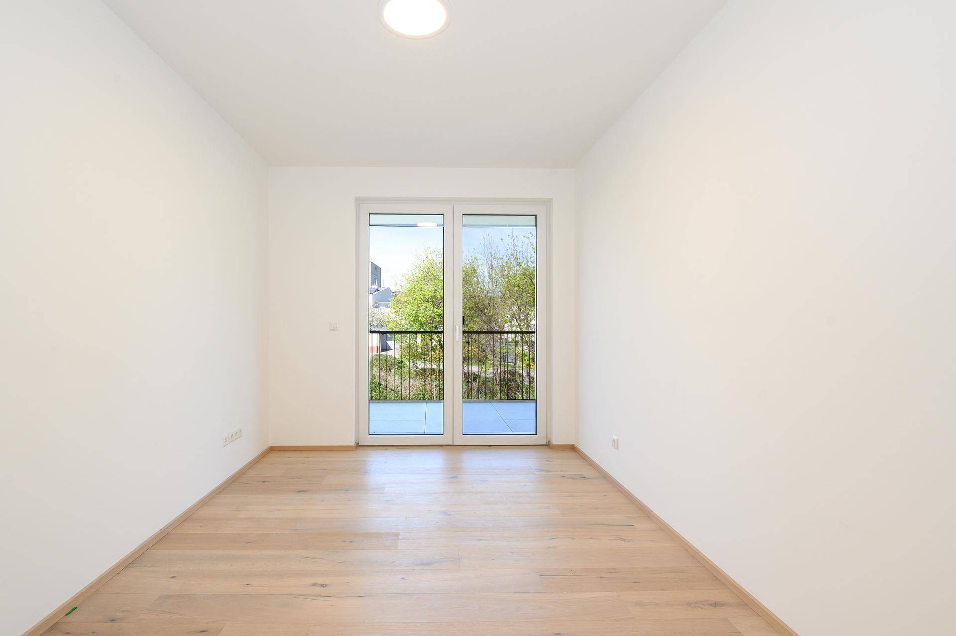 Leeres Zimmer mit hellem Parkettboden und Zugang zu einem französischen Balkon.