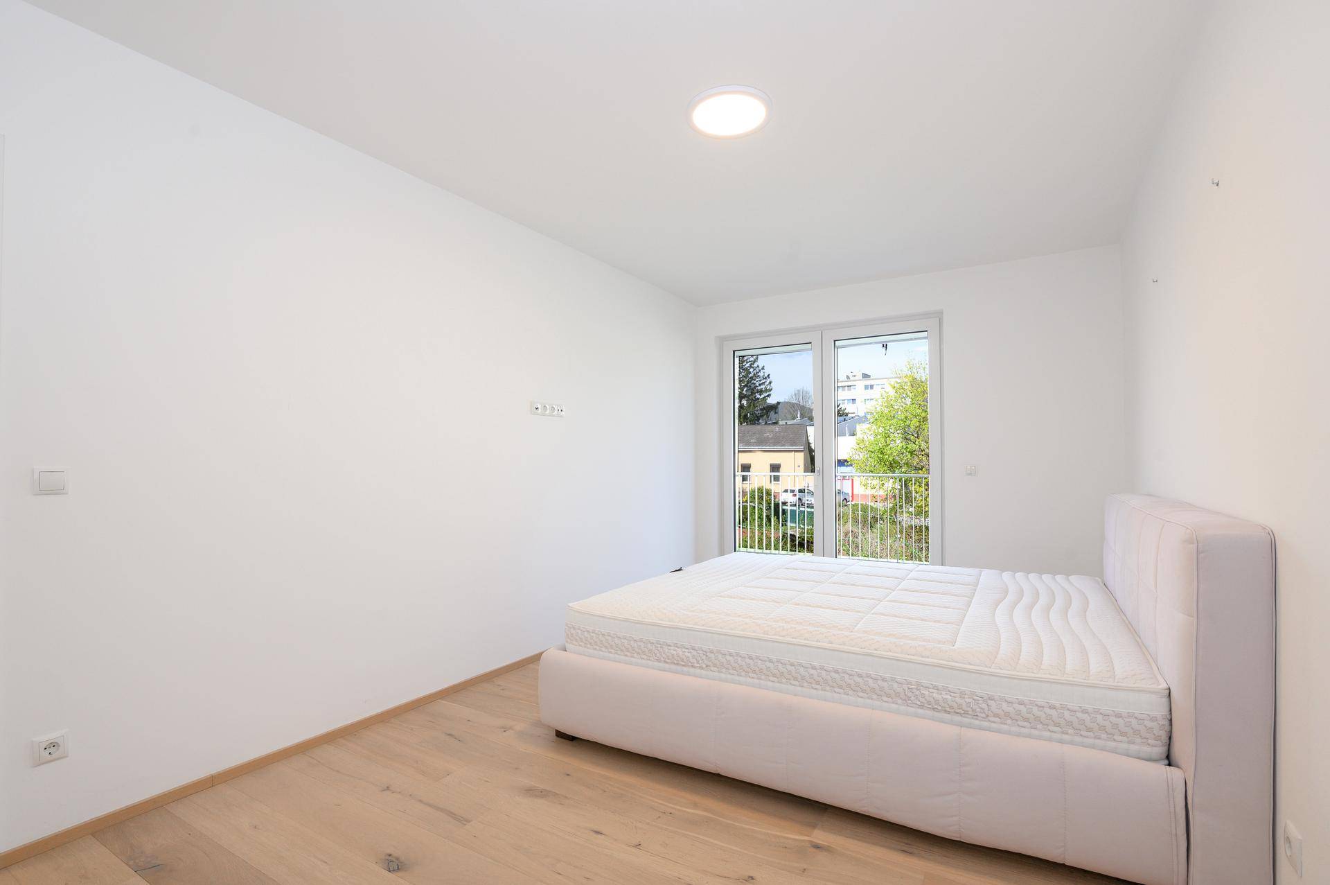 Helles Schlafzimmer mit Doppelbett, Parkettboden und Zugang zu einem Balkon.