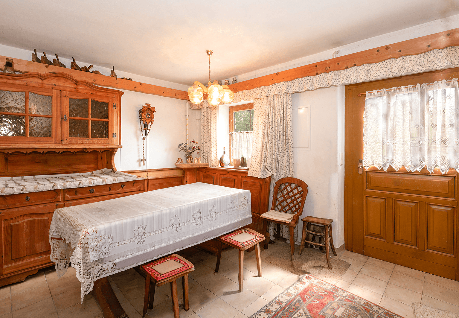 Rustikaler Essbereich mit Holztisch, traditionellen Möbeln und karierten Vorhängen.