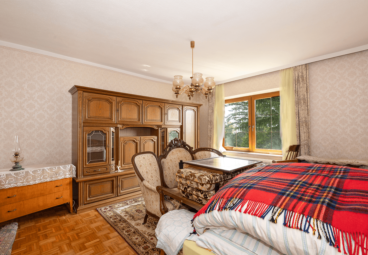 Geräumiges Zimmer mit traditionellen Holzmöbeln, Parkettboden und gemusterter Tapete.
