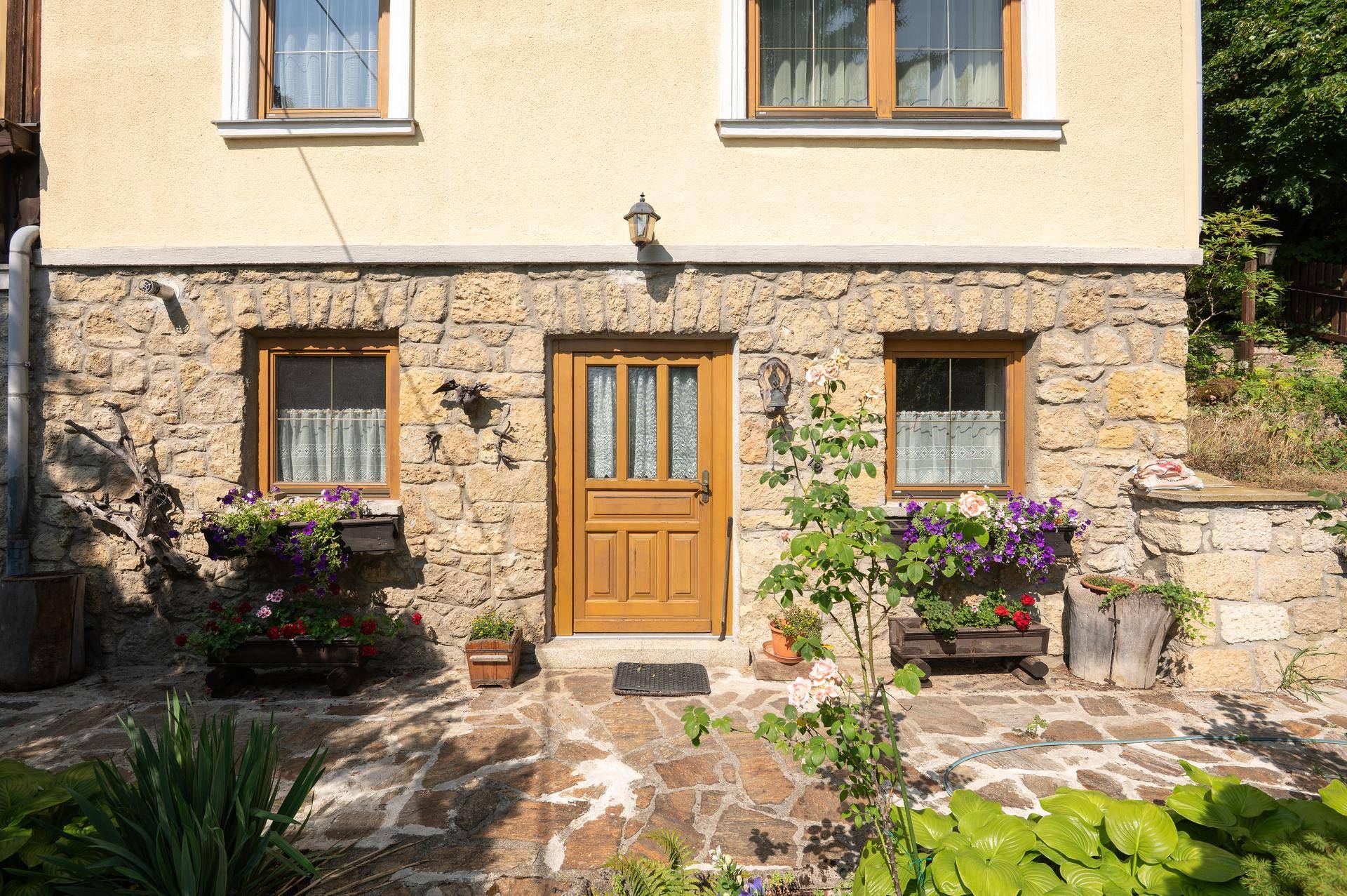 Eingangsbereich des Hauses mit Steinfassade, Holztür und Blumenkästen.
