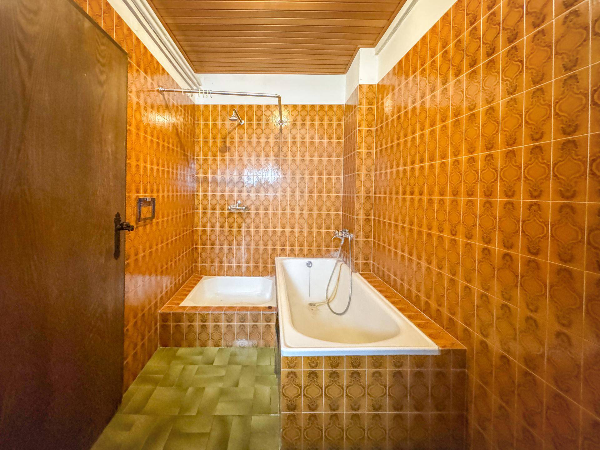 Badezimmer mit orangefarbenen Wandfliesen, grünen Bodenfliesen und Badewanne.