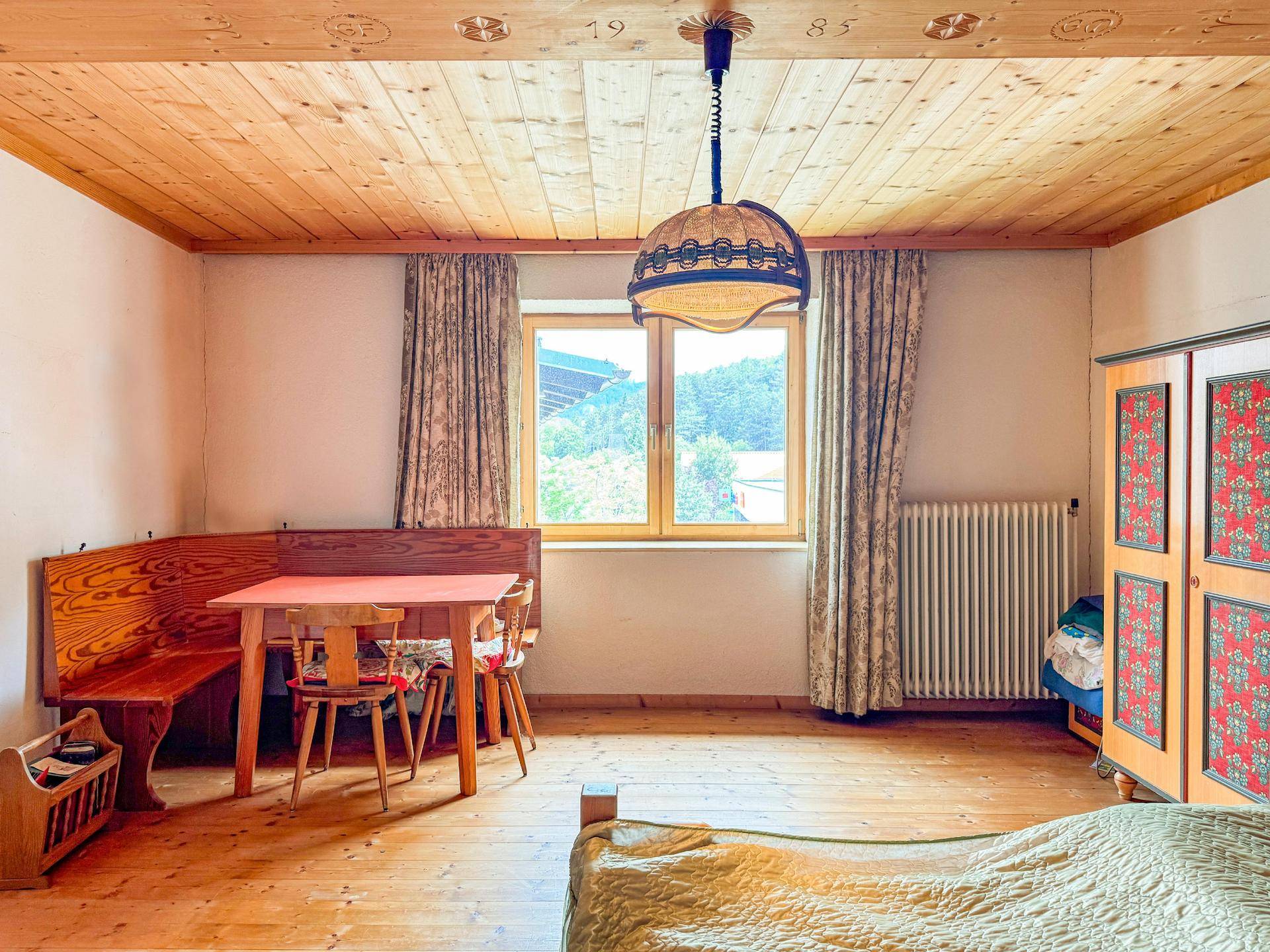 Schlafzimmer mit Holzbalkendecke, traditioneller Sitzecke und Blick ins Grüne.