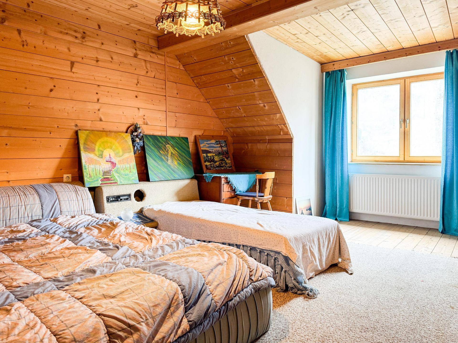 Gemütliches Schlafzimmer im Dachgeschoss mit Holzvertäfelung, Teppichboden und blauen Vorhängen.