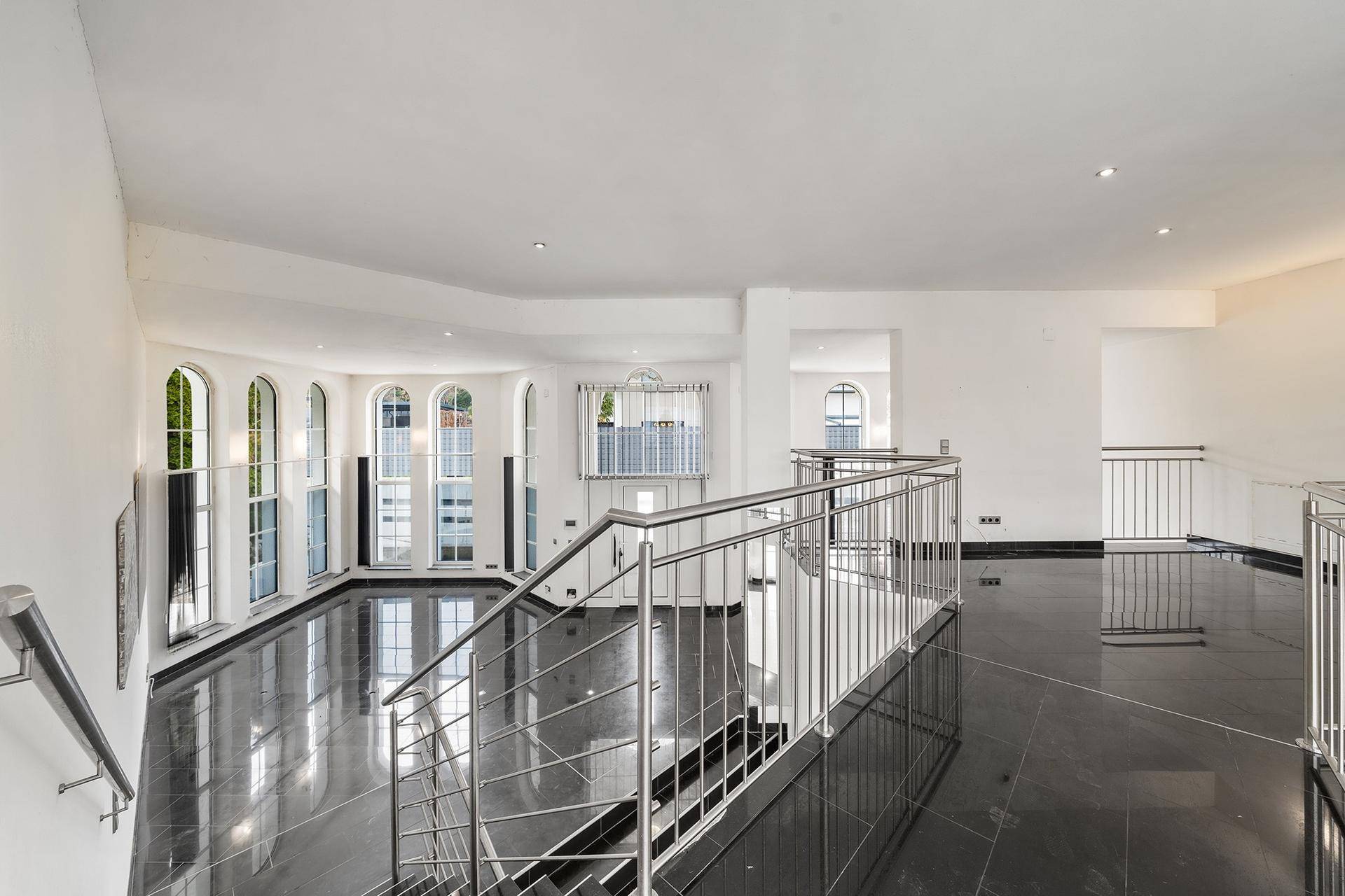 Heller Flur im Obergeschoss mit glänzendem Fliesenboden und moderner Edelstahl-Treppe.