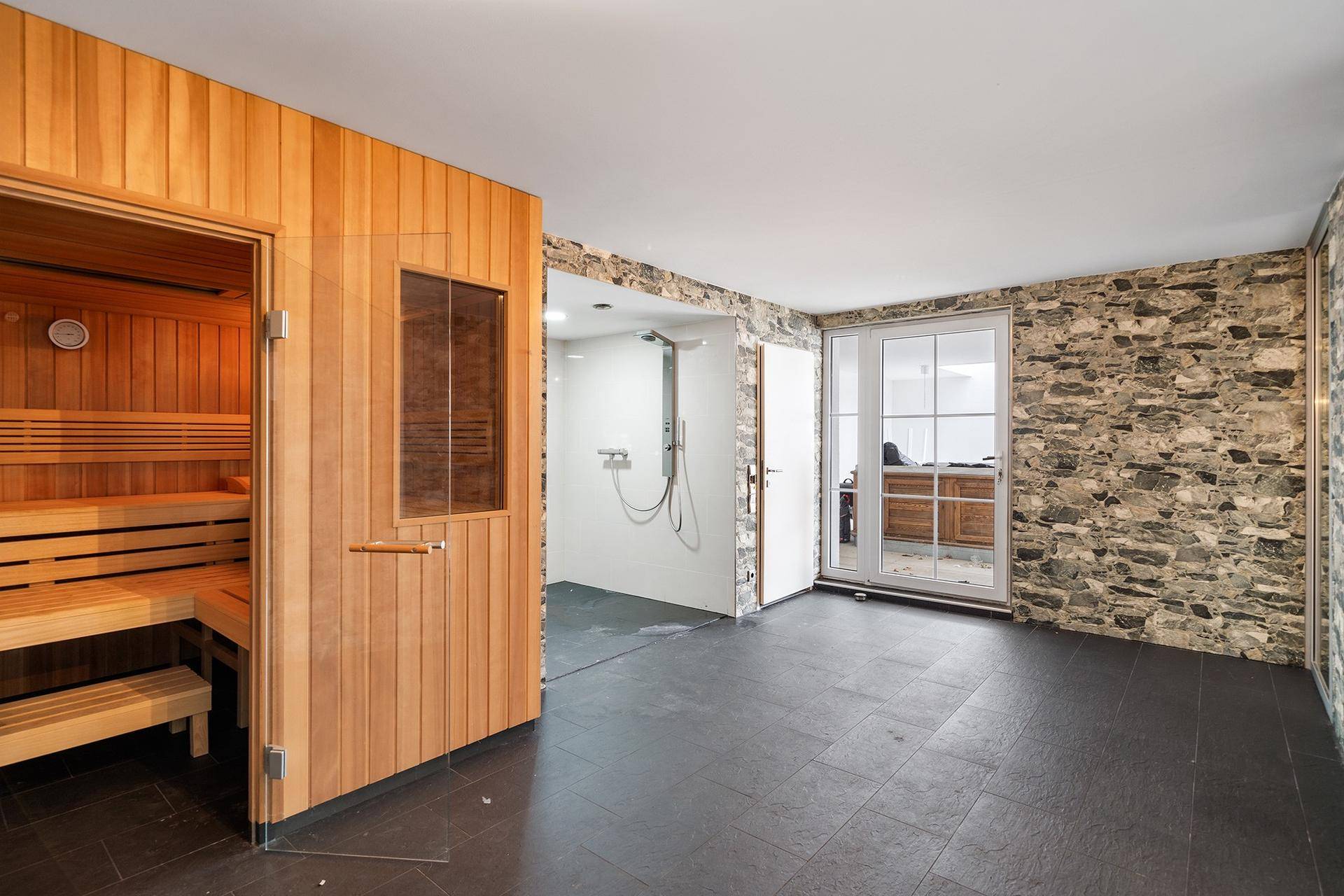Exklusiver Wellnessbereich mit Holzsauna, Regendusche und Natursteinwand.