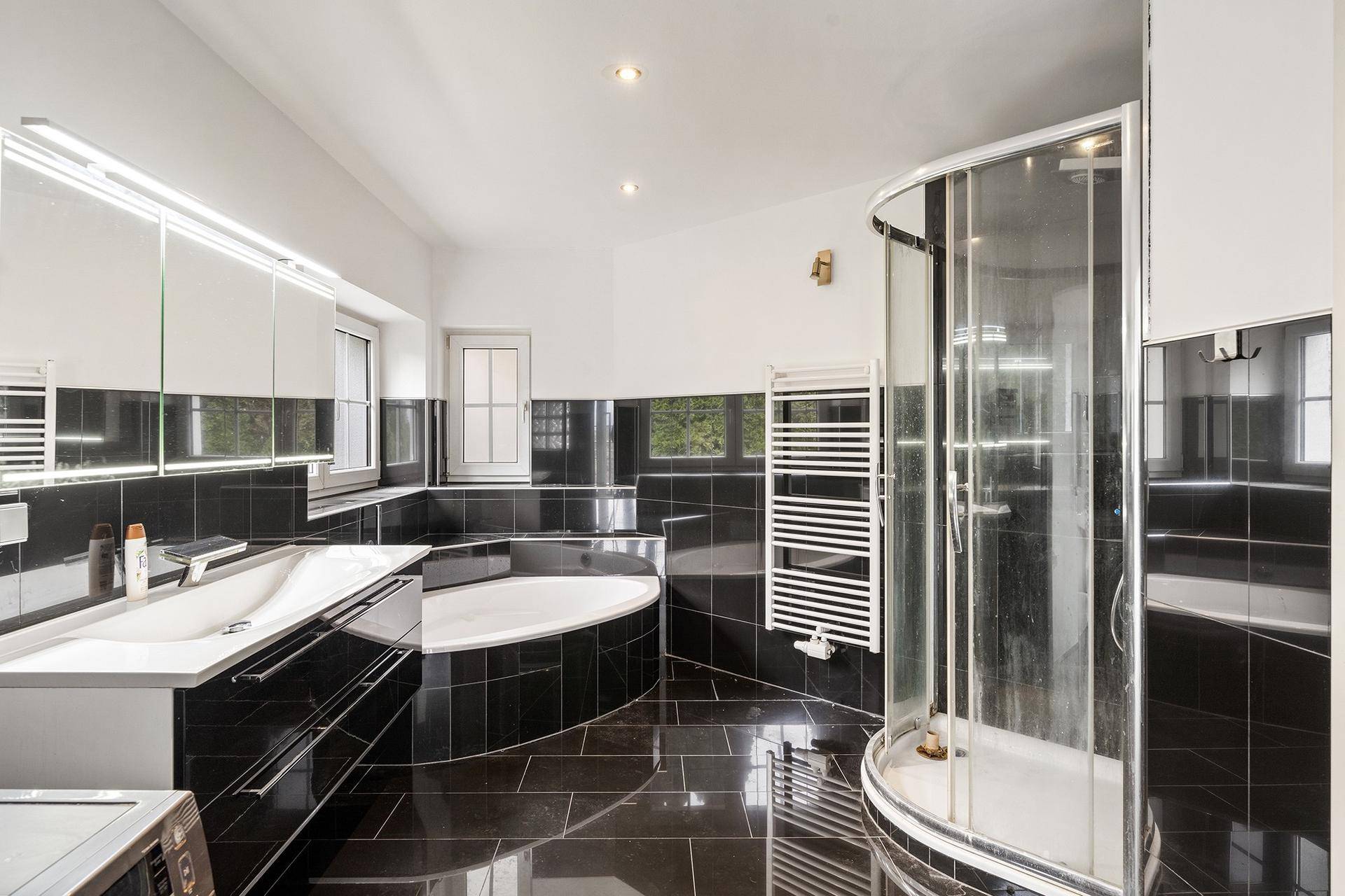 Modernes Badezimmer mit schwarzen Fliesen, runder Dusche und großer Eckbadewanne.