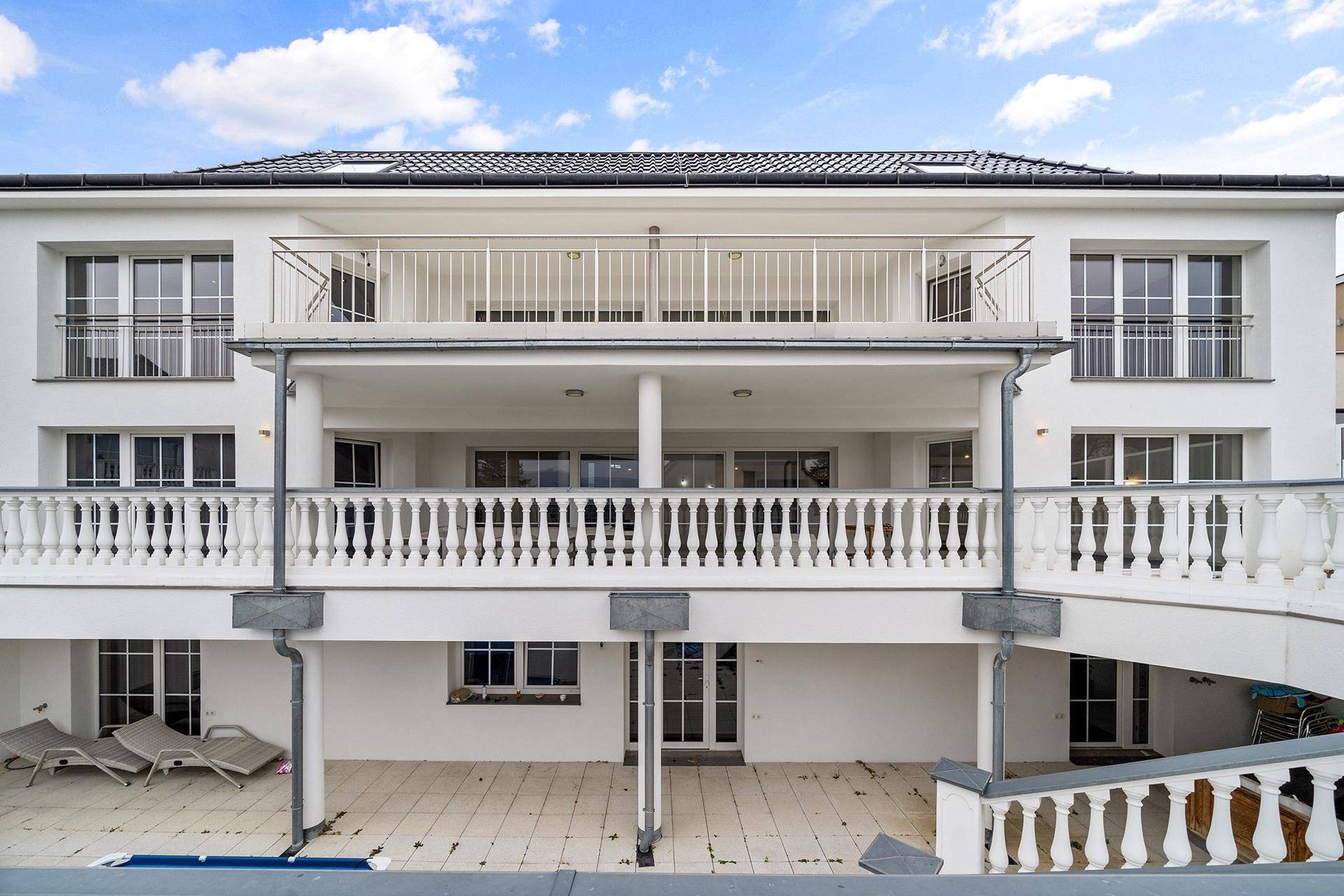 Elegante weiße Fassade eines modernen Gebäudes mit mehreren Balkonen und Terrassen.