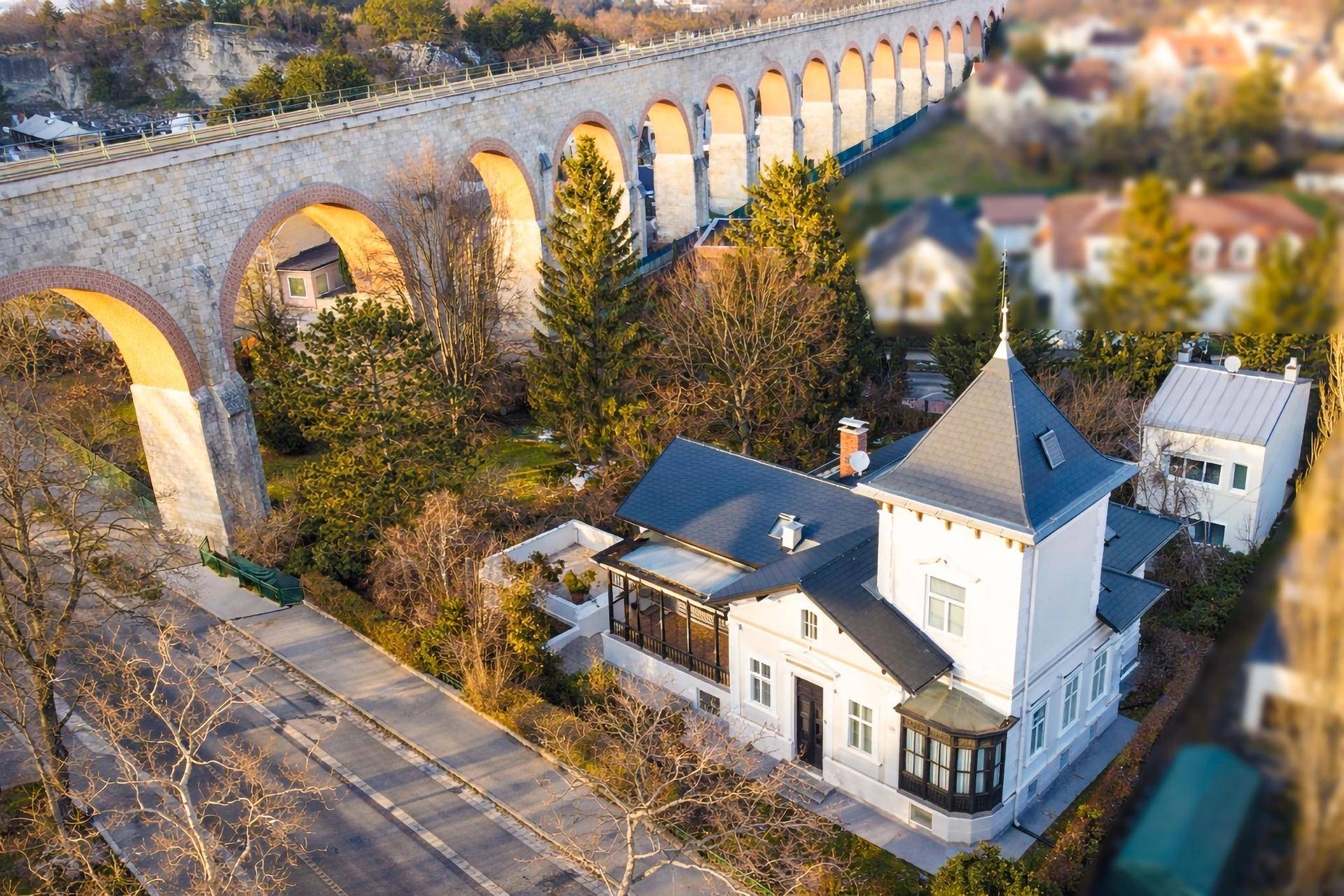 Luftaufnahme einer historischen Villa neben einem imposanten Viadukt in grüner Umgebung.