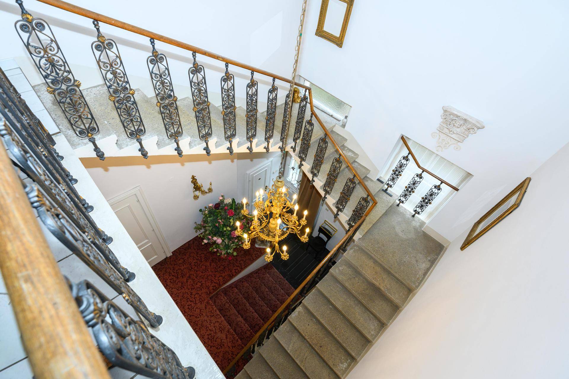 Elegantes Treppenhaus mit schmiedeeisernem Geländer und einem opulenten Kronleuchter.