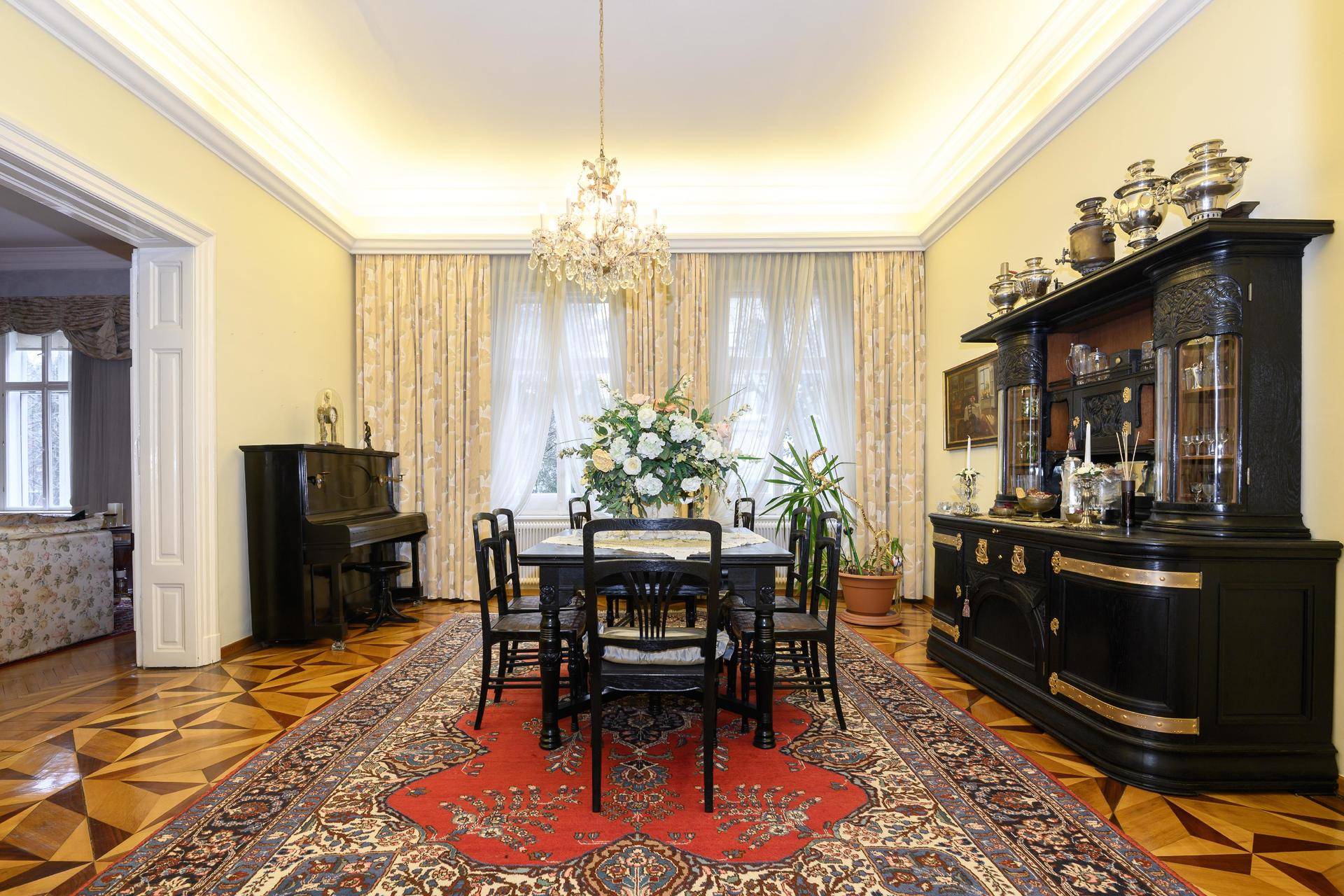 Elegantes Esszimmer mit prunkvollem Kronleuchter, Parkettboden und antiken Möbeln.