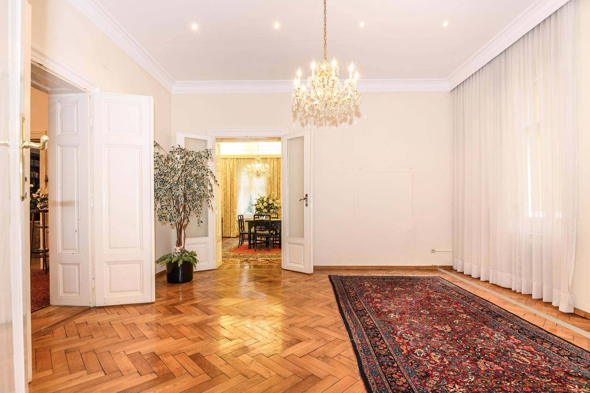 Großzügiges Wohnzimmer mit Fischgrätparkett, hohen Decken und Blick in den Essbereich.