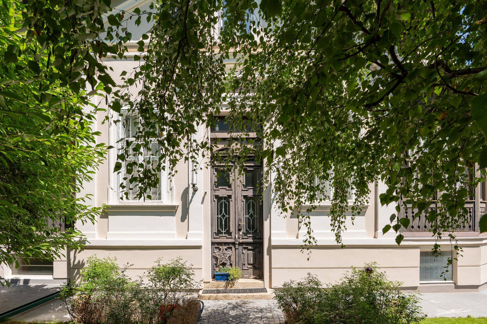 Prunkvoller Eingangsbereich der historischen Villa, umgeben von Bäumen und Sträuchern.