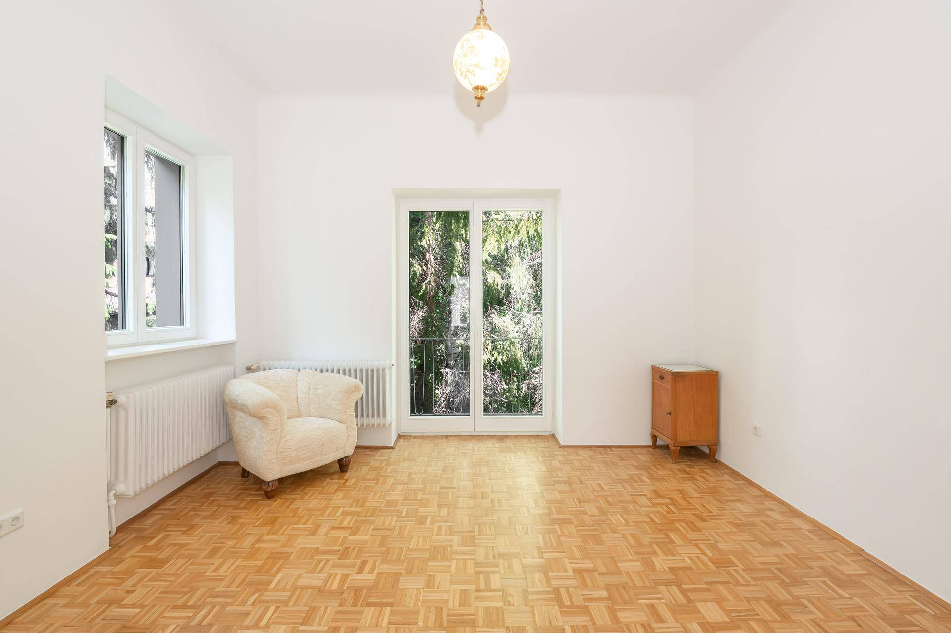 Helles Zimmer mit Parkettboden, weiß gestrichenen Wänden und Zugang zu einem französischen Balkon.