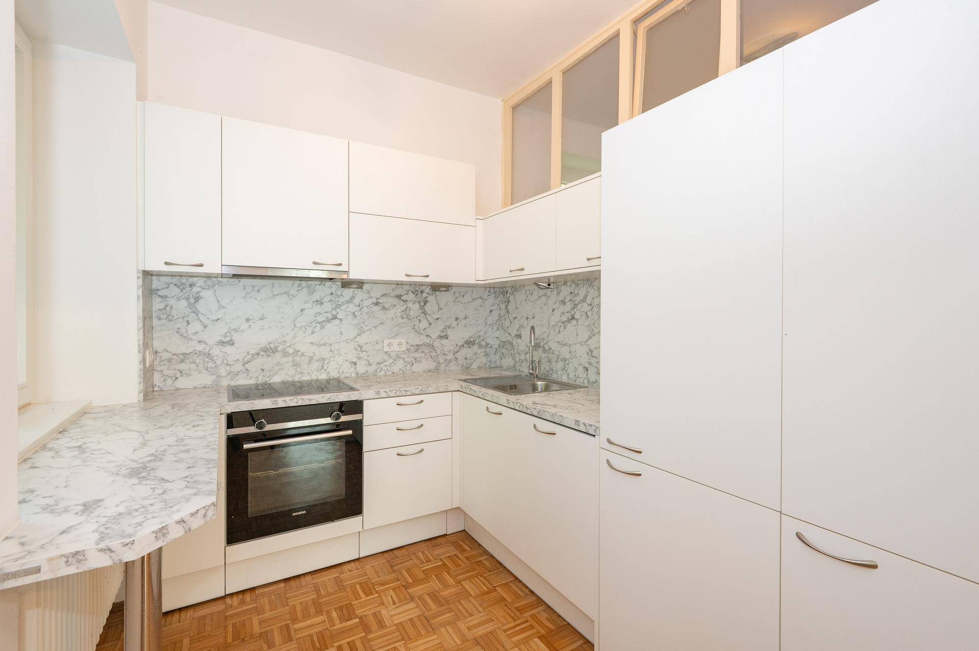 Moderne weiße Küche mit Einbaugeräten, Marmor-Arbeitsplatten und Parkettboden.