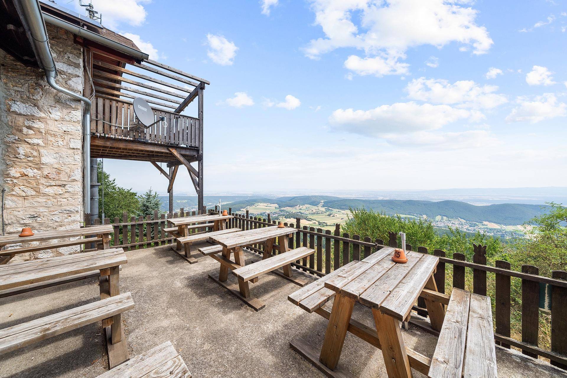 Rustikale Terrasse mit Holzbänken und Tischen, ideal für Mahlzeiten im Freien mit Panoramablick.