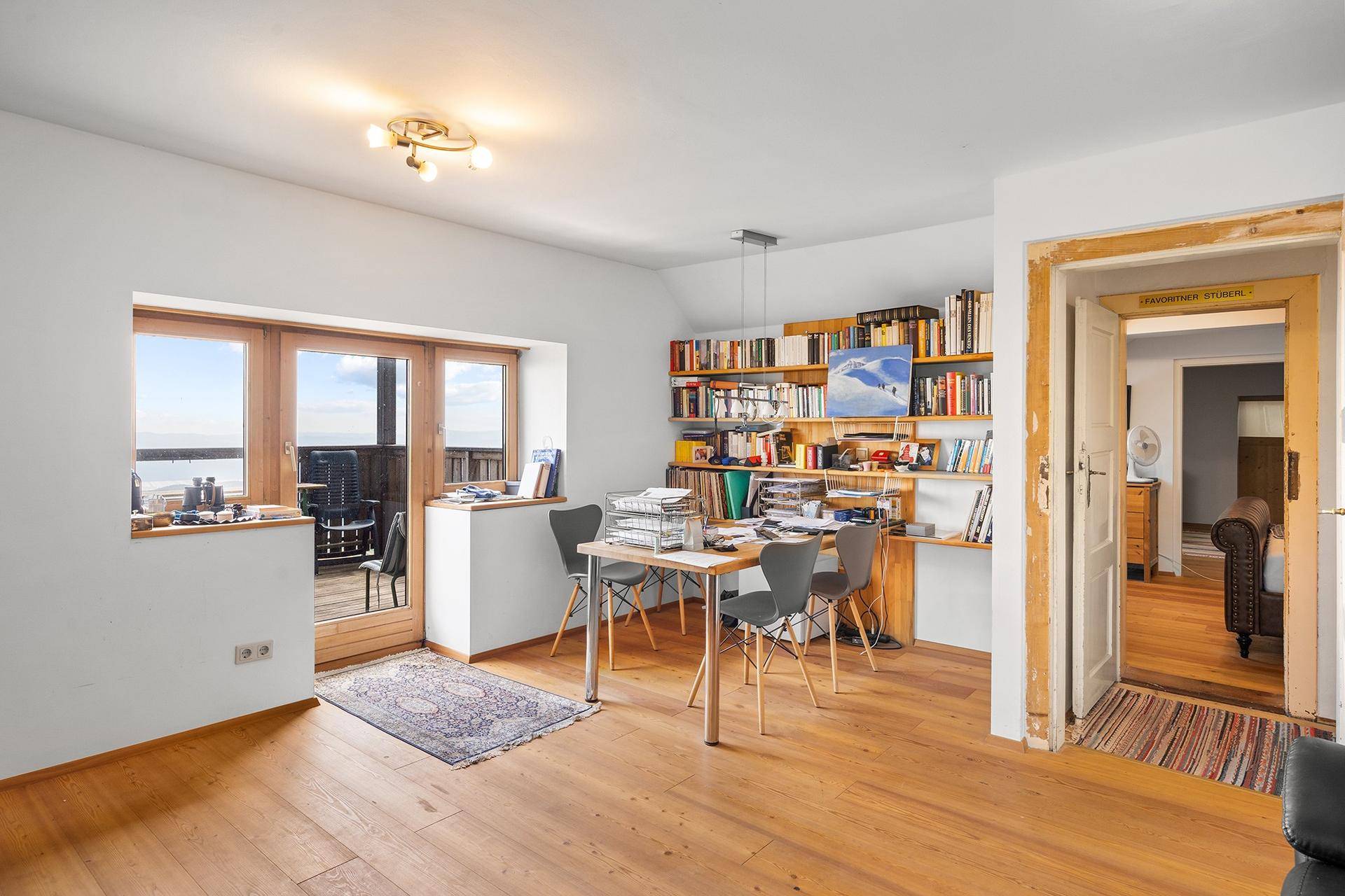 Helles Arbeitszimmer mit Holzboden, Bücherregalen und Zugang zu einem Balkon mit Aussicht.