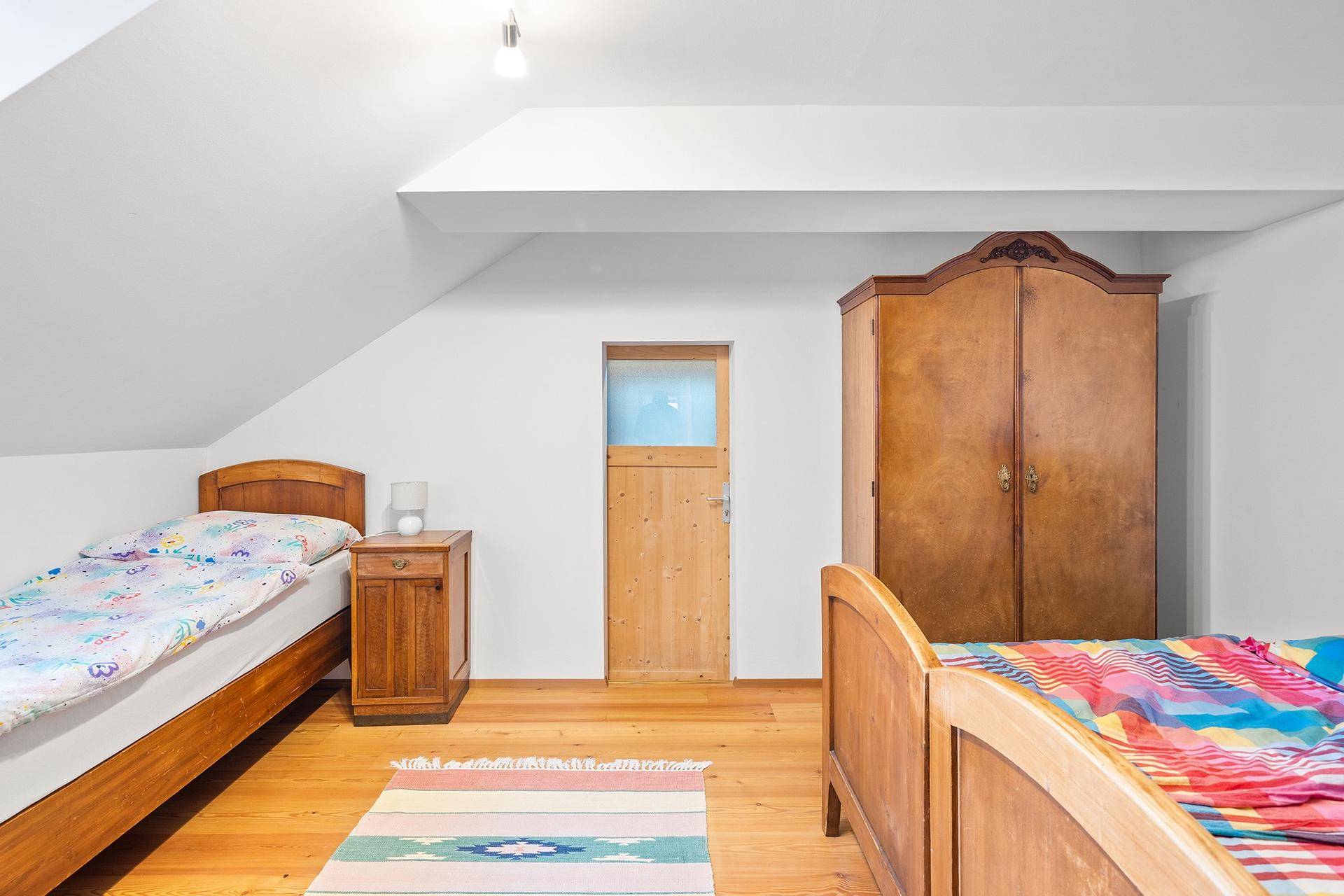 Gemütliches Schlafzimmer mit zwei Einzelbetten, Holzmöbeln und schrägen Decken.