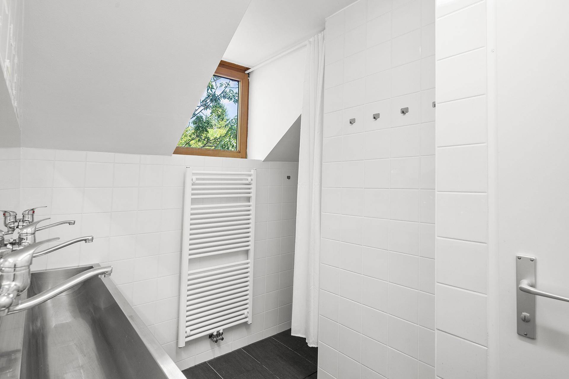 Funktionales Badezimmer mit weiß gefliesten Wänden, großem Waschbecken und beheiztem Handtuchhalter.